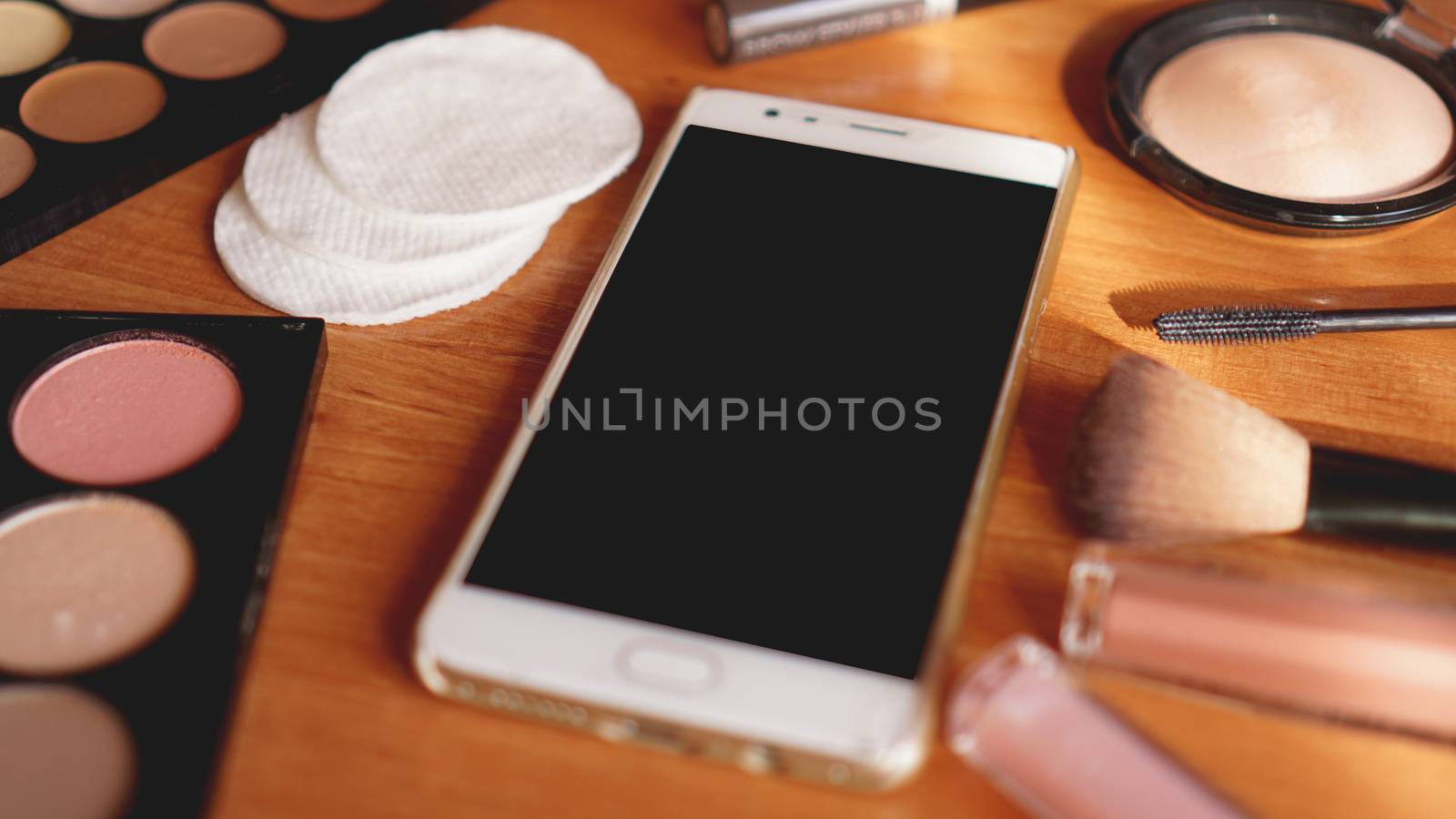 Smartphone with empty screen and cosmetics on light wooden background. Top view, flat lay. Mobile phone mockup.