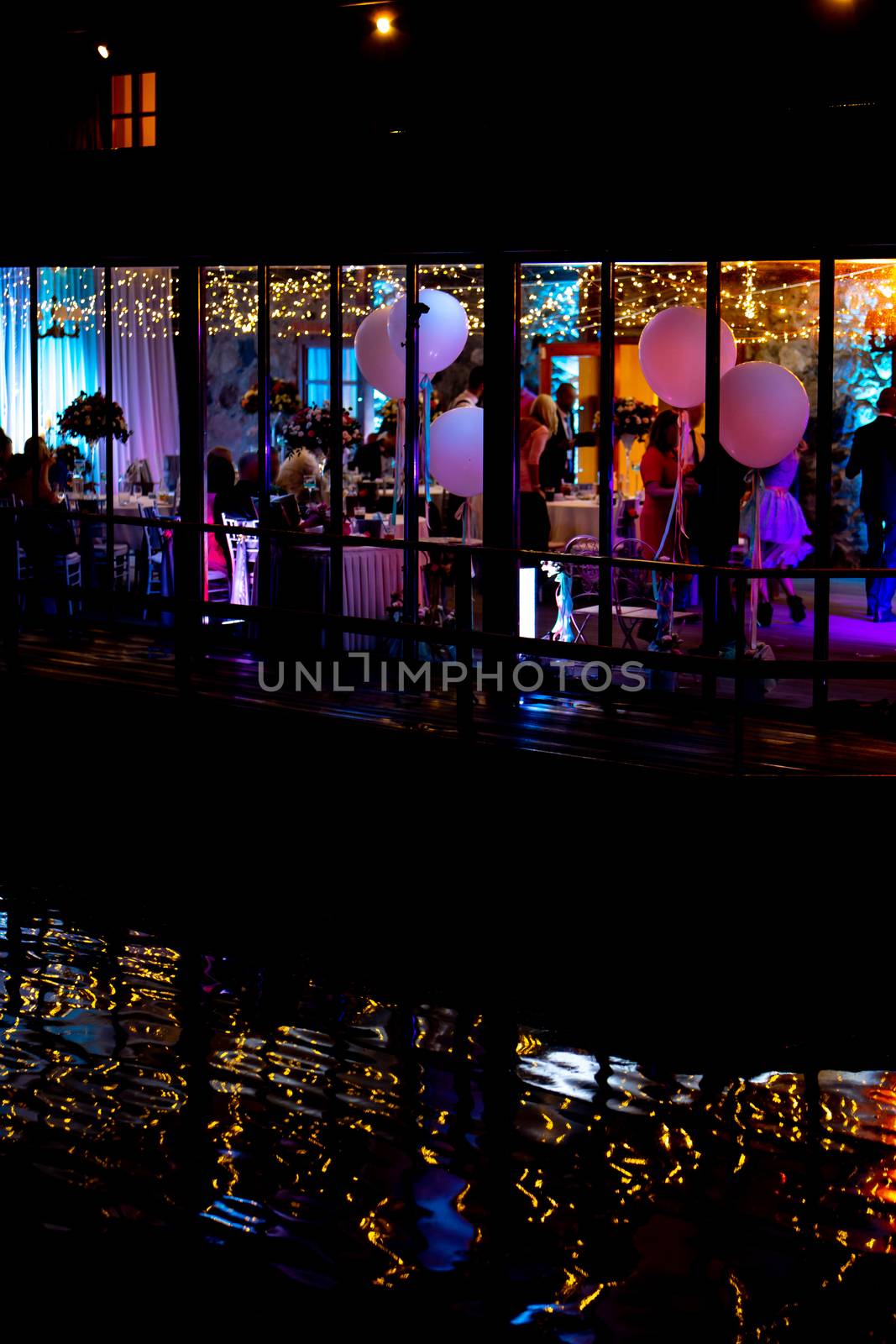 Silhouettes of people in the window during wedding celebrations at night, in the light of colorful spotlights.