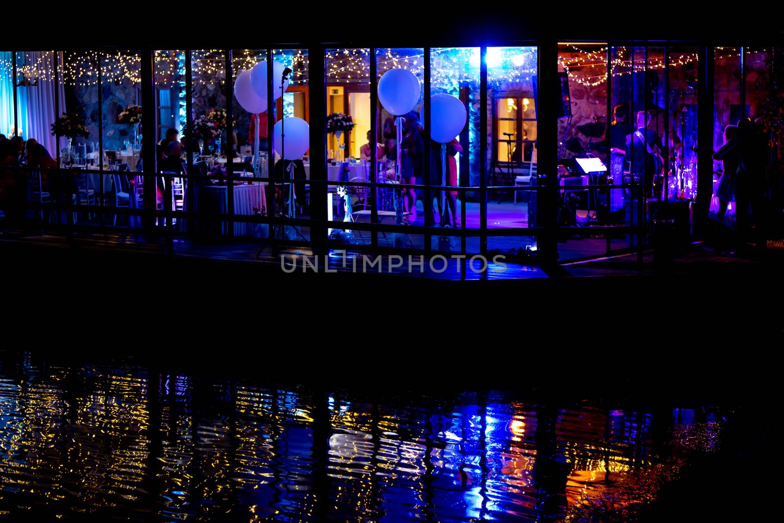 Silhouettes of people in the window during wedding celebrations at night, in the light of colorful spotlights.