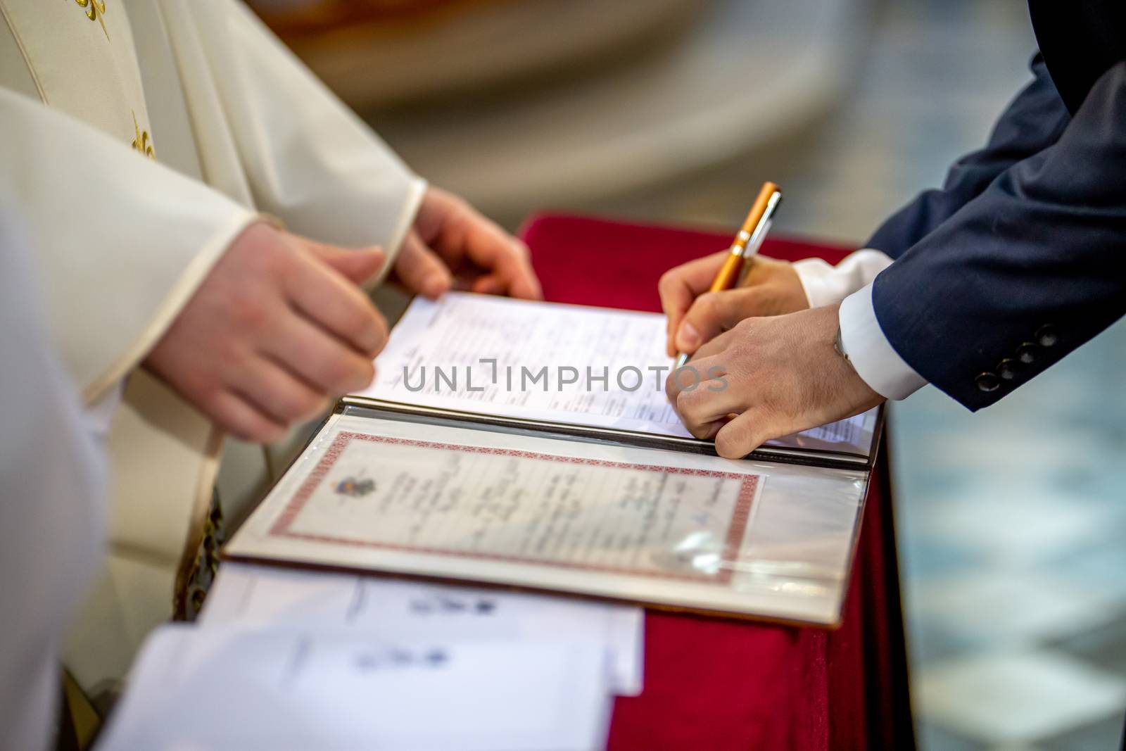 The groom signs documents on registration of marriage in the presence of the pastor. Young couple signs wedding documents in the church during wedding ceremony, Latvia