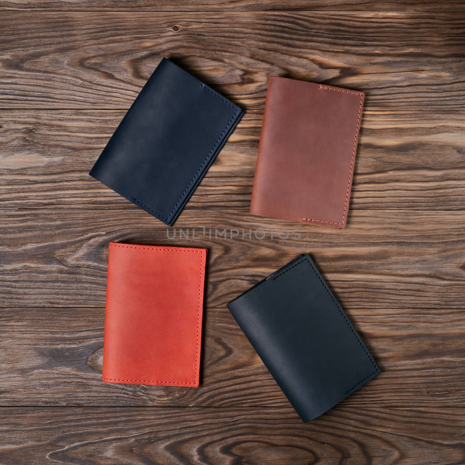Four handmade leather passport covers on wooden textured background. Black, red, ginger and brown covers. Up to down view. Stock photo of luxury accessories.