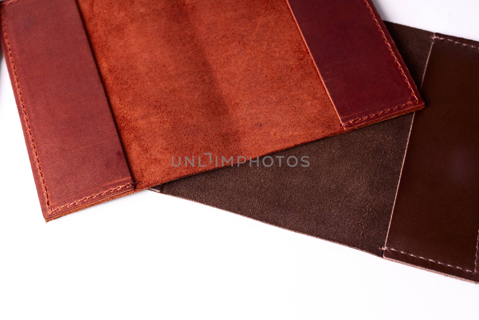 Two handmade leather passport covers isolated on white background. Closeup view. Covers are red, brown and open.