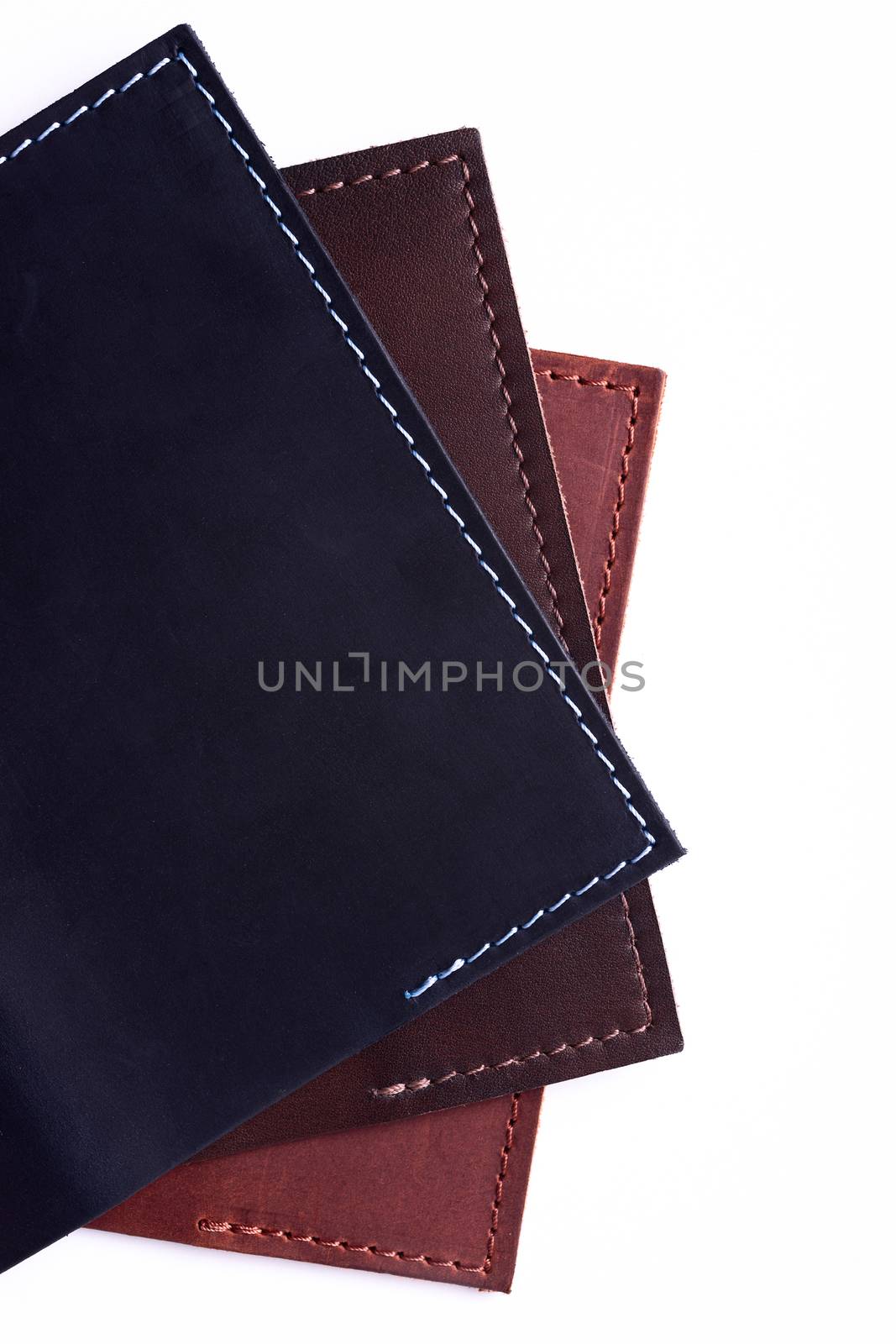 A parts of three handmade leather passport covers isolated on white background. Closeup view. Covers are dark blue, red and brown.
