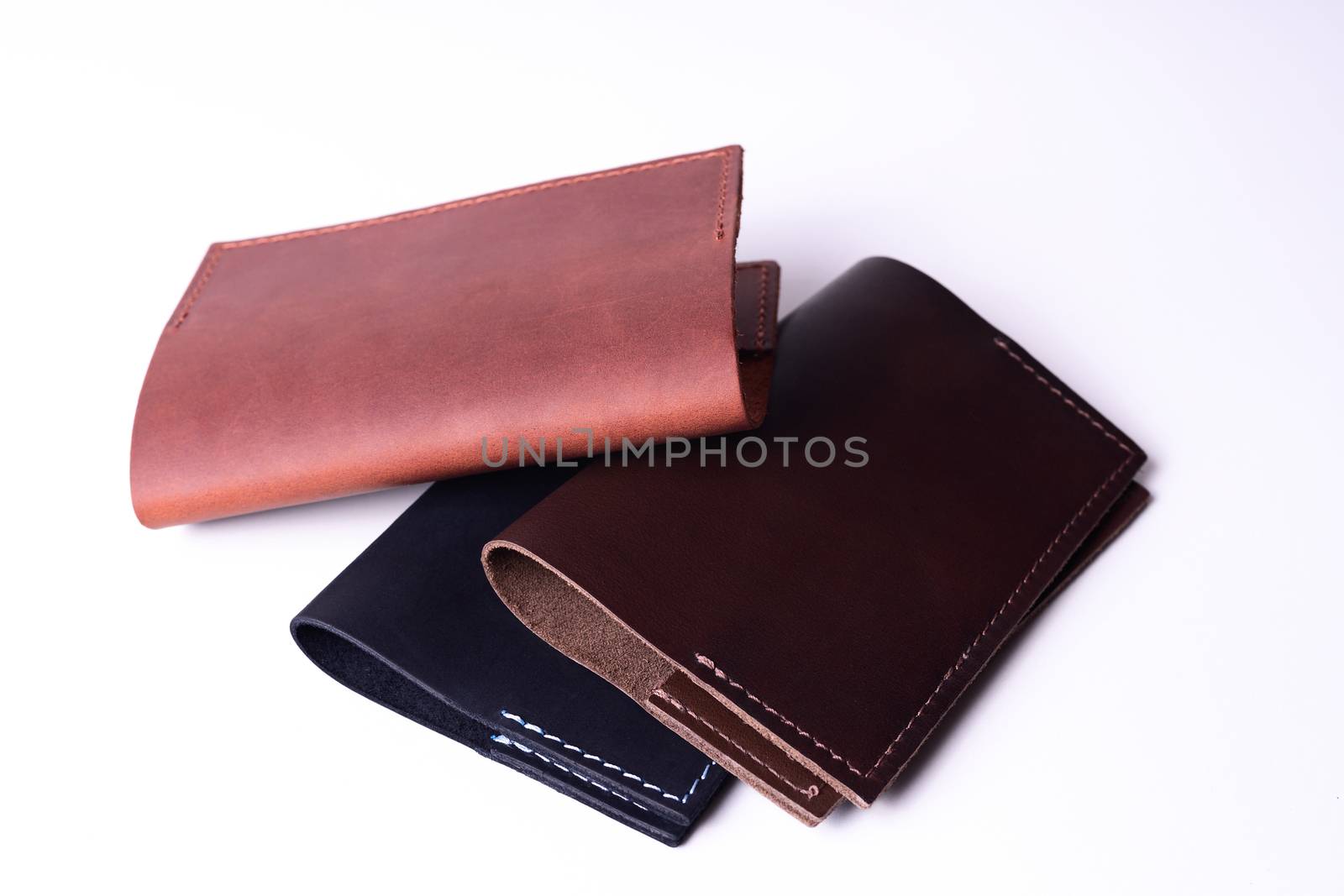 Three handmade leather passport covers isolated on white background. Covers are closed. Closeup view. Covers are dark blue, red and brown.