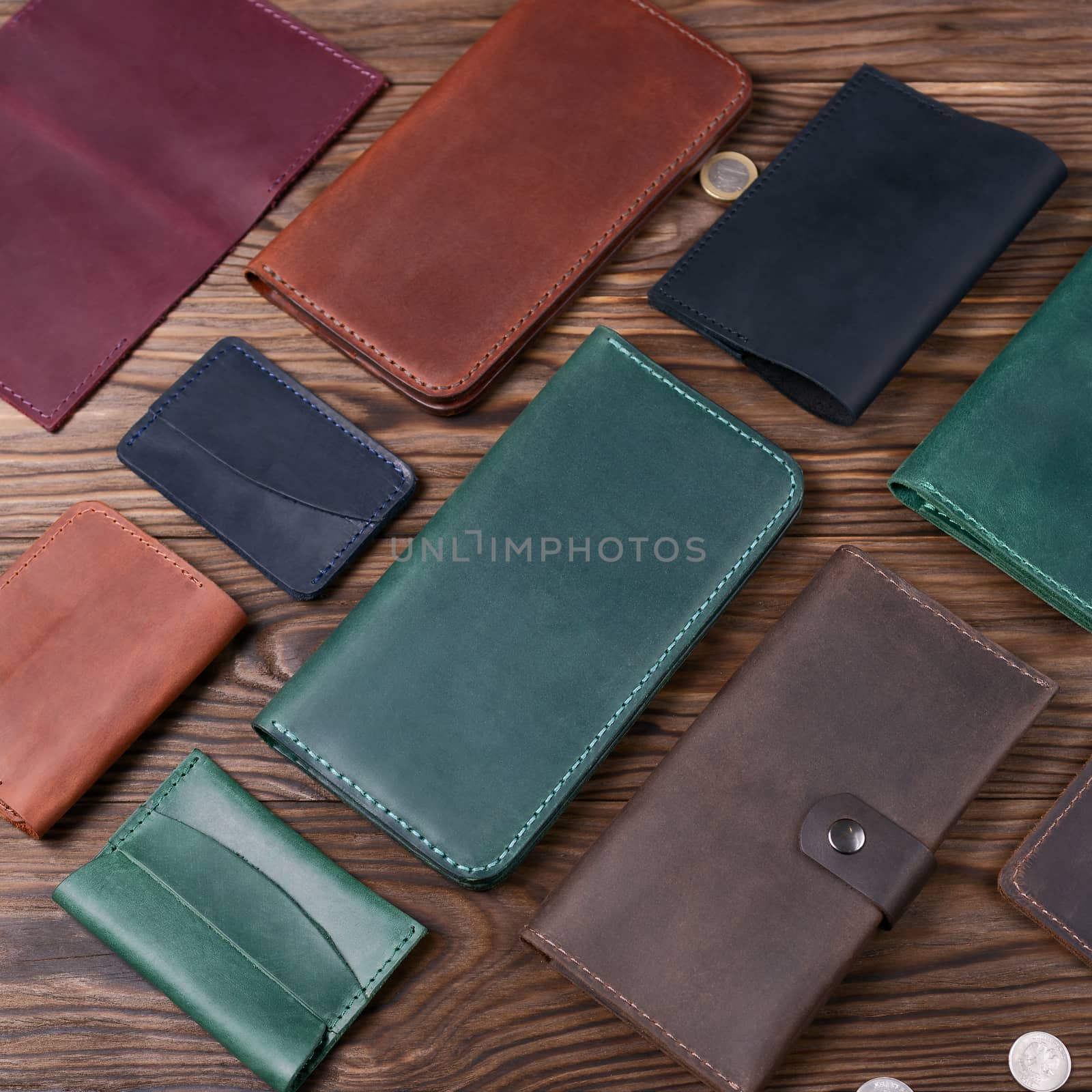Green color handmade leather porte-monnaie surrounded by other leather accessories on wooden textured background.  Side view. Stock photo of luxury accessories.