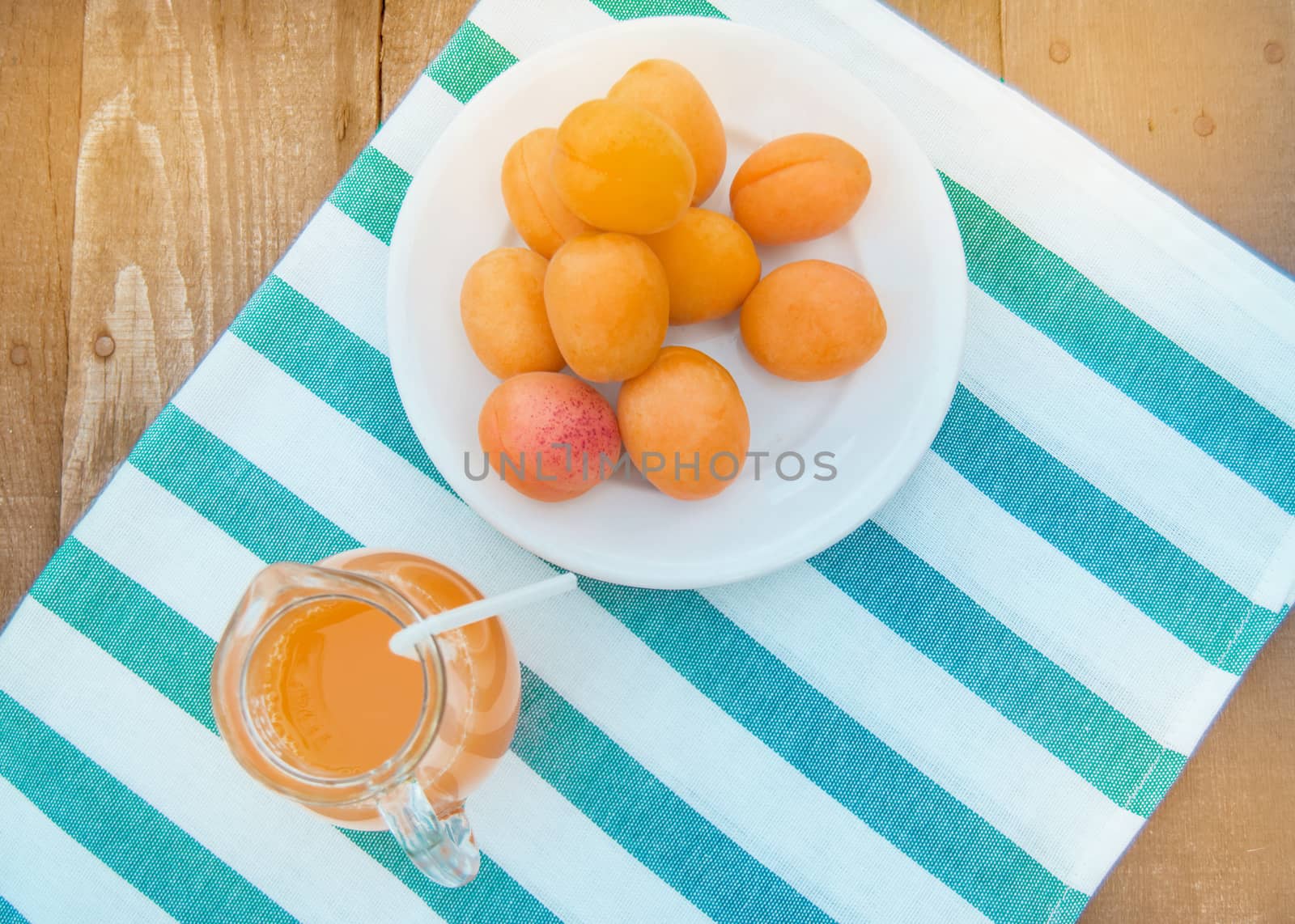 Summer drink and fruit-fresh apricot juice in a glass jug and ripe apricots on a napkin, top view, outdoor.