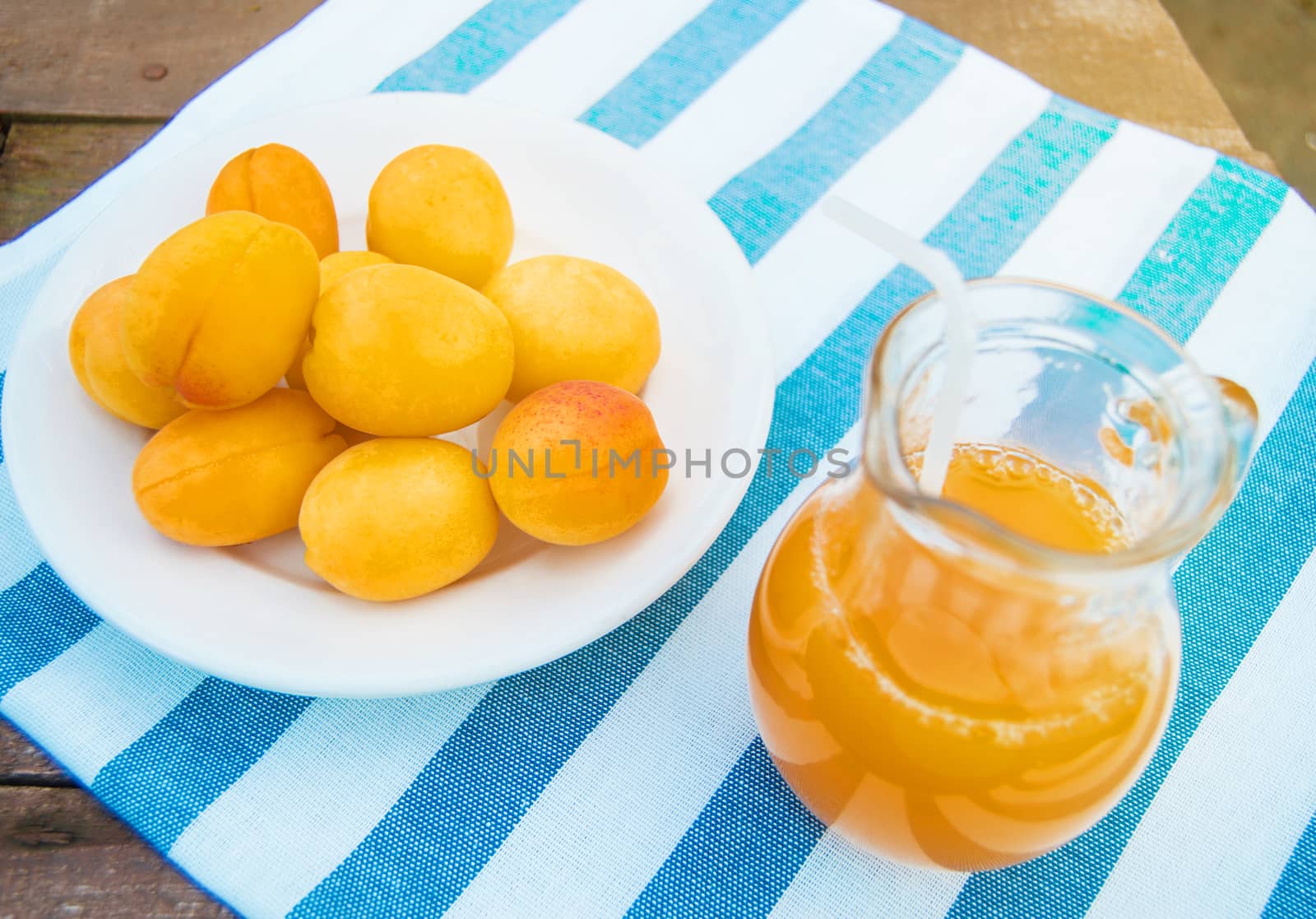 Summer drink and fruit-fresh apricot juice in a glass jug and ripe apricots on a napkin, outdoors on a Sunny day.