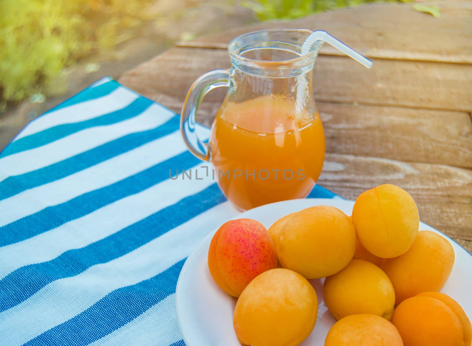 Summer drink and fruit-fresh apricot juice in a glass jug and ripe apricots on a napkin, outdoors on a Sunny day by claire_lucia