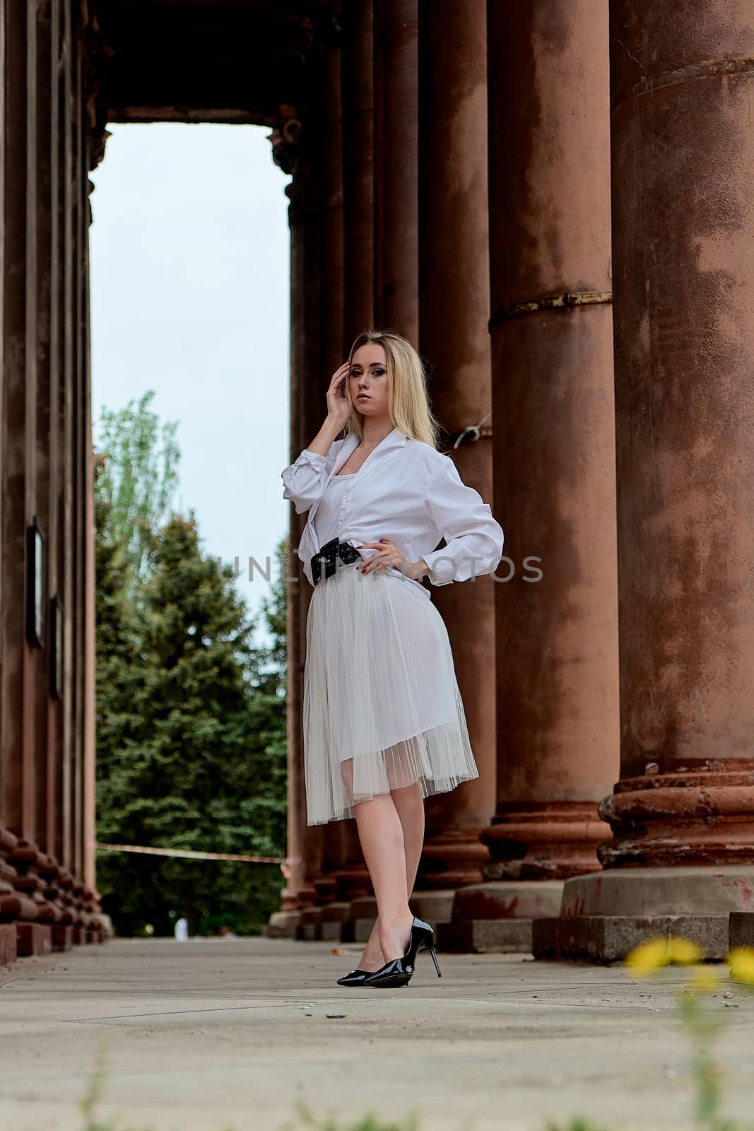 Fashion look's woman. Young woman modern portrait. Young woman dressed in white skirt and shirt posing near the old looking soviet union's architectural building with large pillars and bas-reliefs.