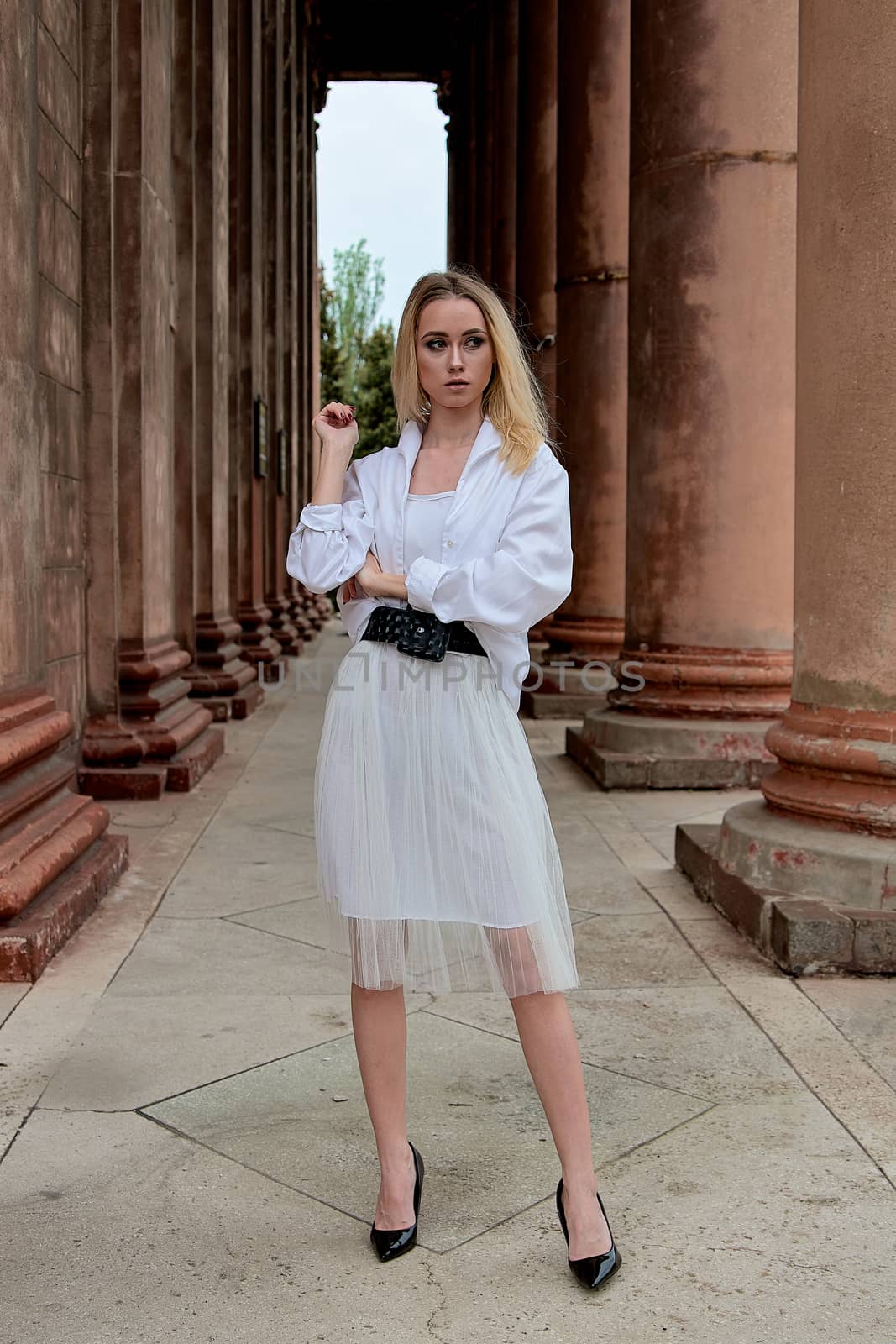 Fashion look's woman. Young woman modern portrait. Young woman dressed in white skirt and shirt posing near the old looking soviet union's architectural building with large pillars and bas-reliefs.