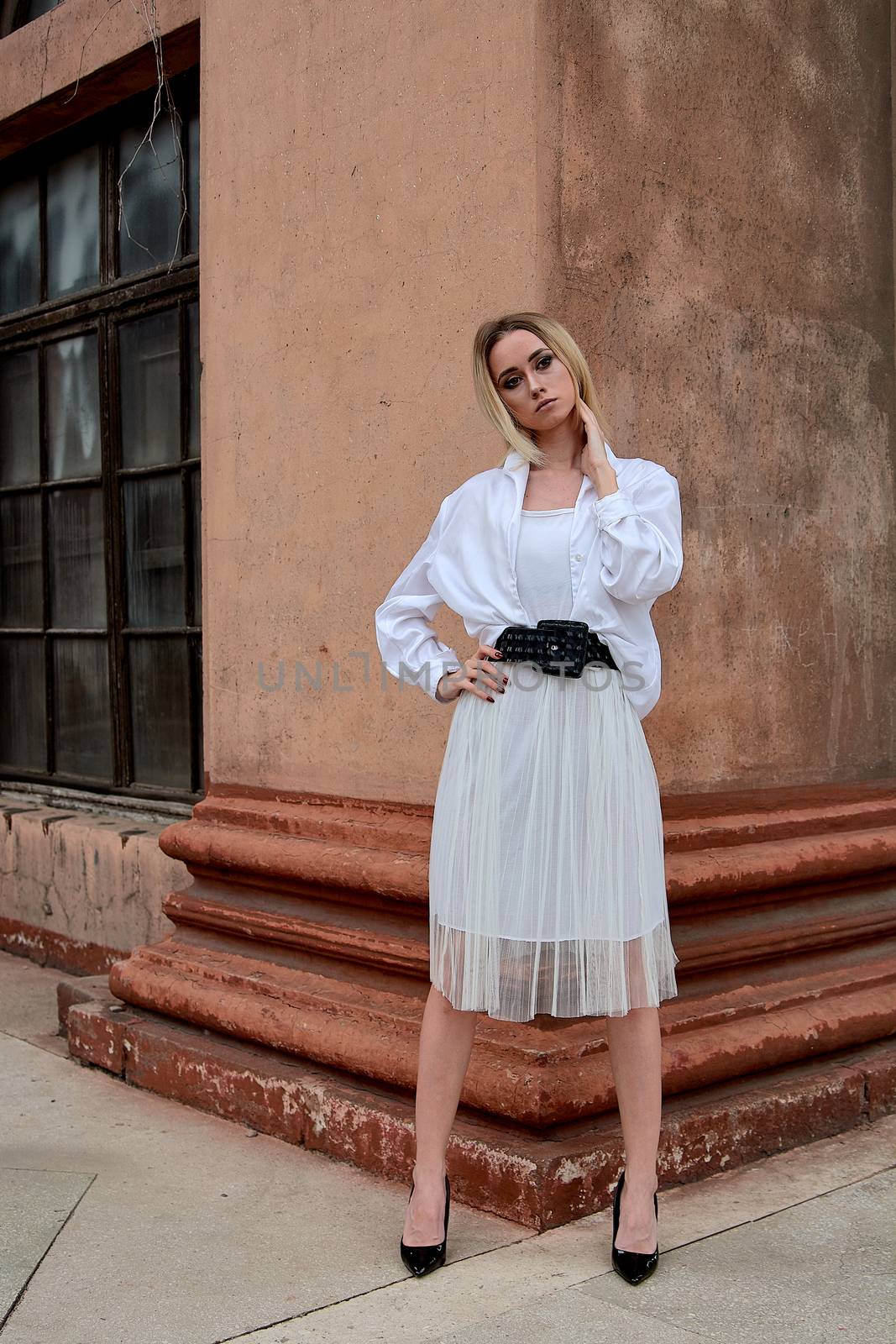Fashion look's woman. Young woman modern portrait. Young woman dressed in white skirt and shirt posing near the old looking soviet union's architectural building with large pillars and bas-reliefs.