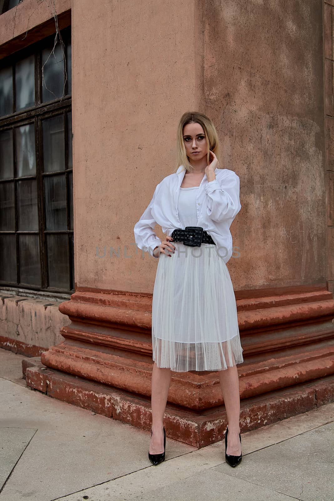 Fashion look's woman. Young woman modern portrait. Young woman dressed in white skirt and shirt posing near the old looking soviet union's architectural building with large pillars and bas-reliefs.