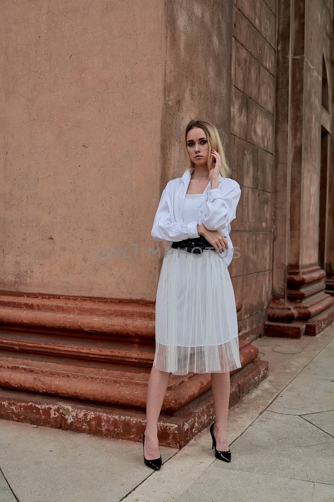 Fashion look's woman. Young woman modern portrait. Young woman dressed in white skirt and shirt posing near the old looking soviet union's architectural building with large pillars and bas-reliefs.