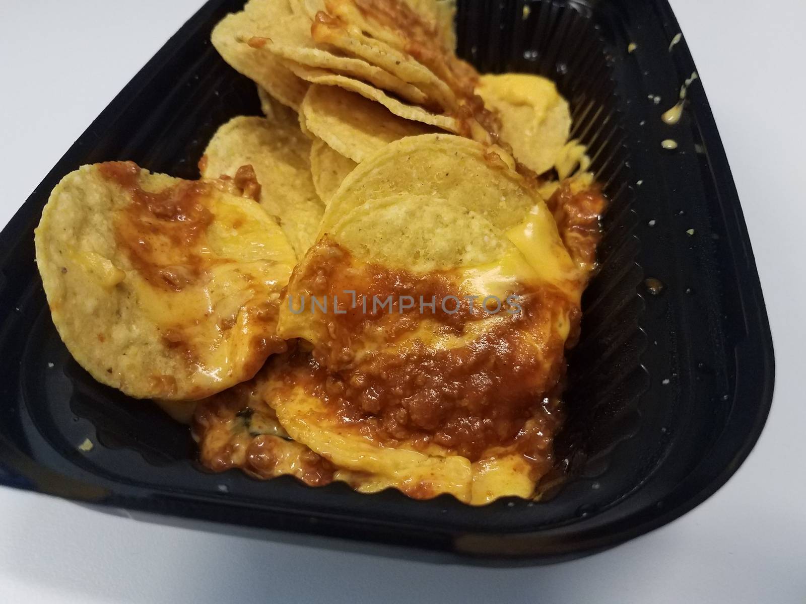 tortilla chips with cheese and meat sauce in black plastic container by stockphotofan1