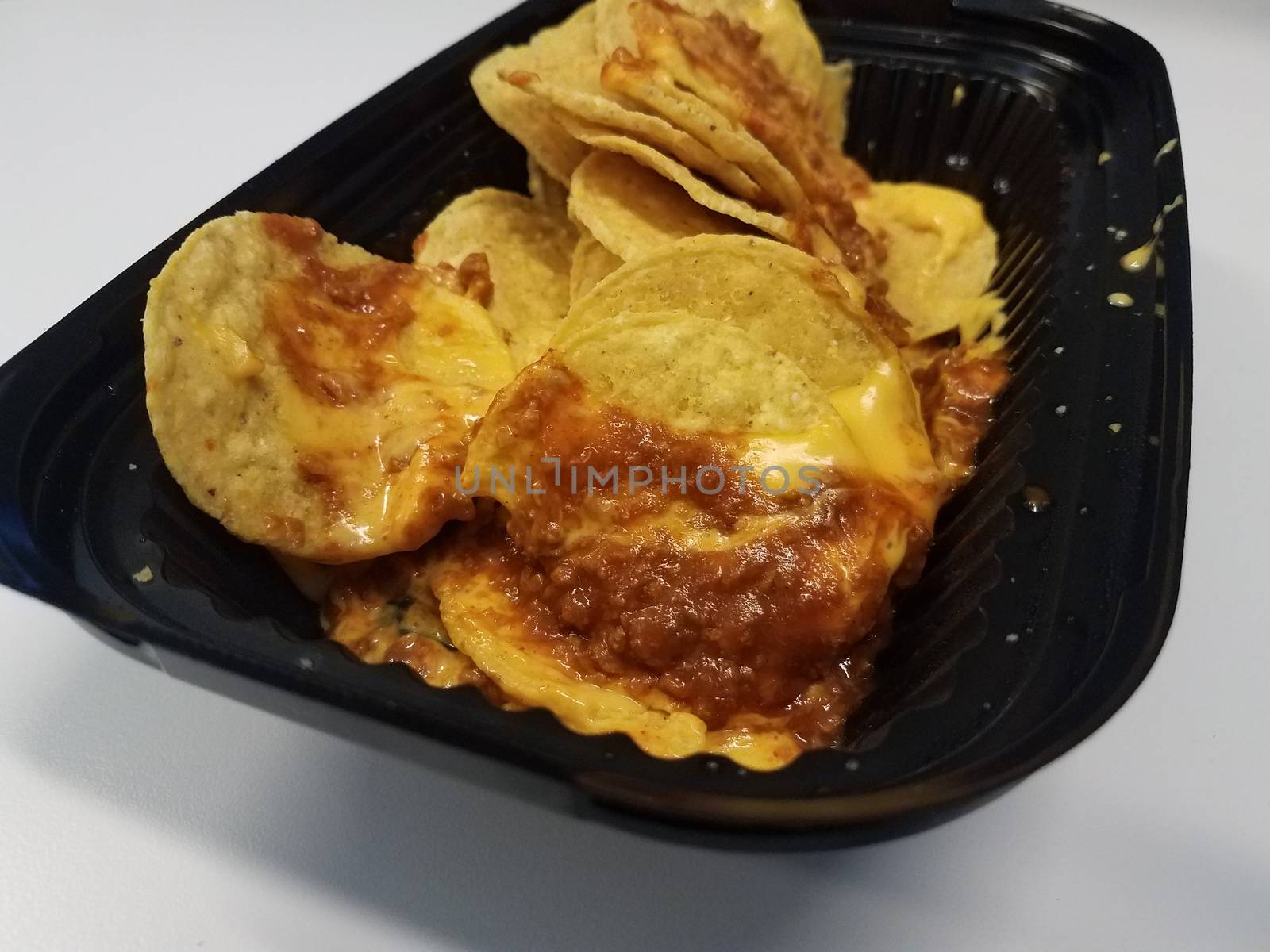 tortilla chips with cheese and meat sauce or nachos in black plastic container