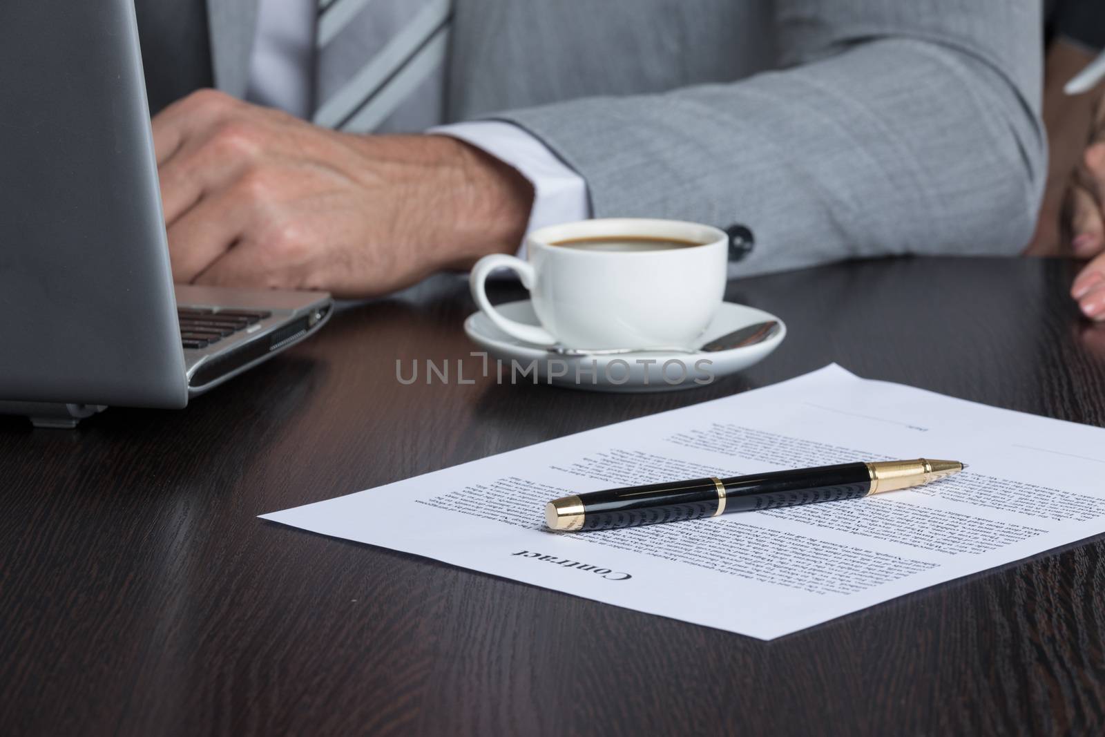 Close up photo of businessman sitting at office desk in front of laptop and working with contract document