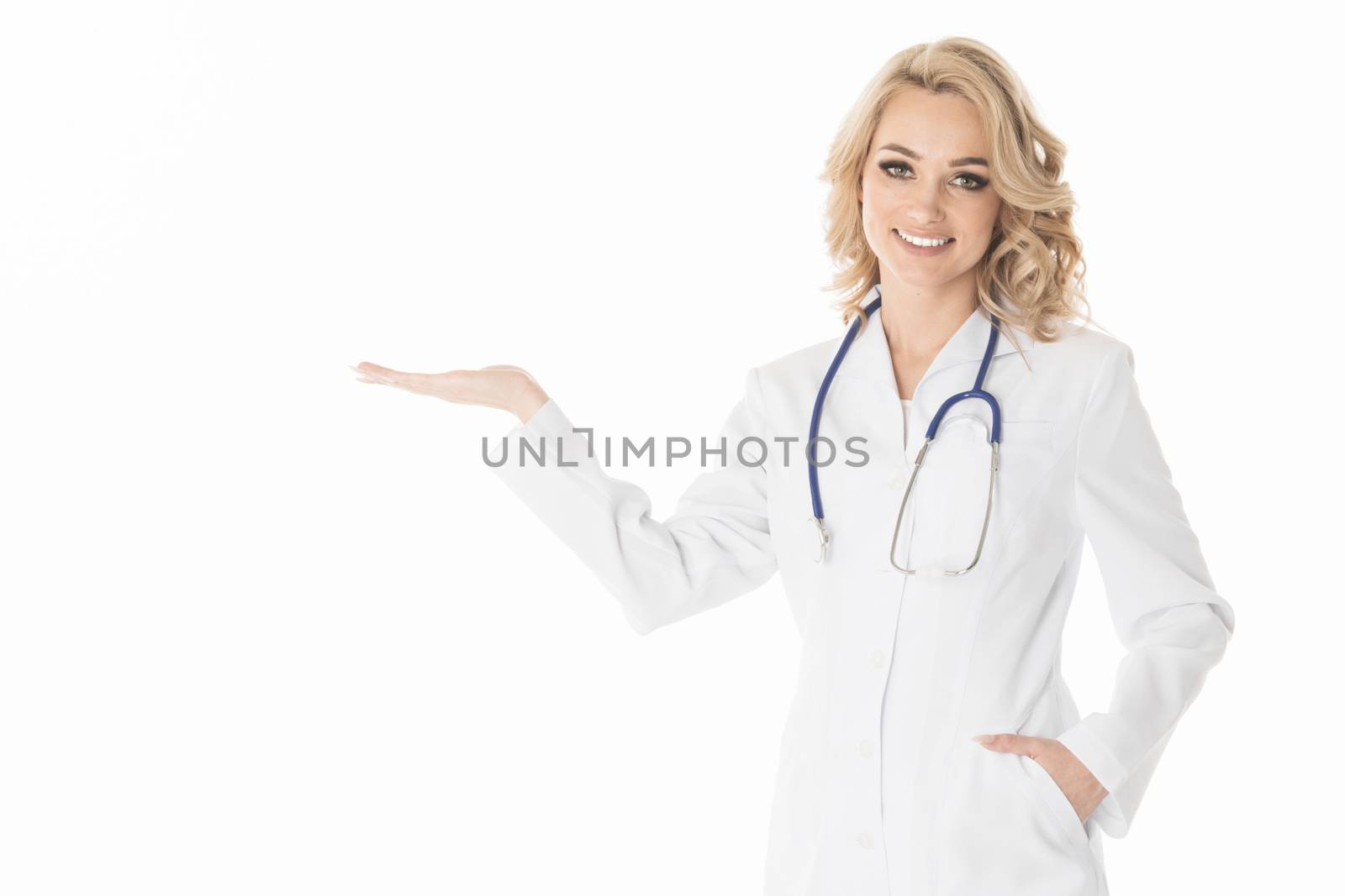 Smiling female doctor in white coat pointing with hand palm at empty copy space, studio isolated on white background