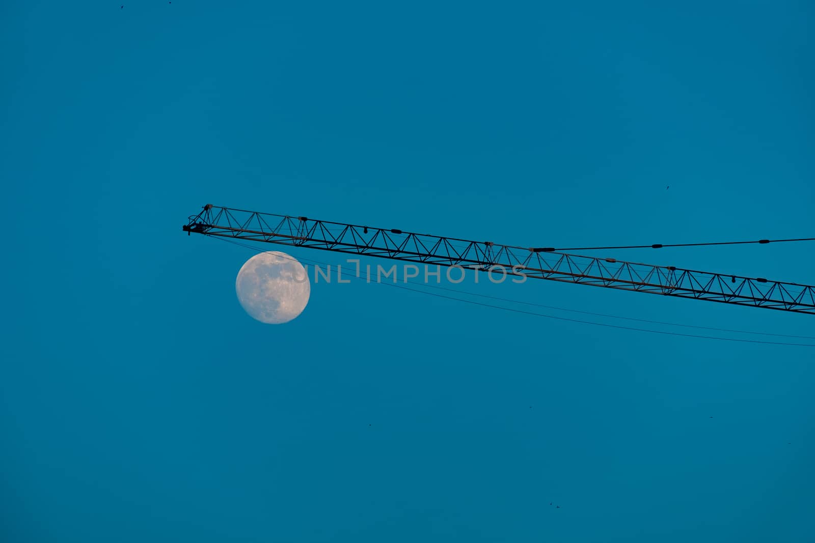 Crane on a construction site against blue sky and a moon