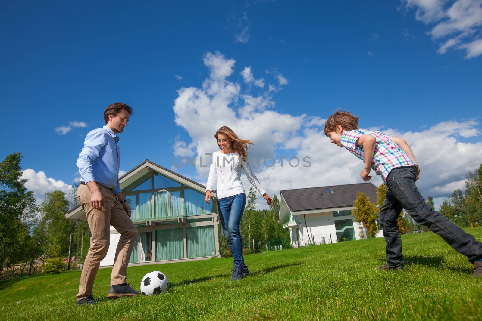 Family with of parents and son playing football on the backyard lawn near their house