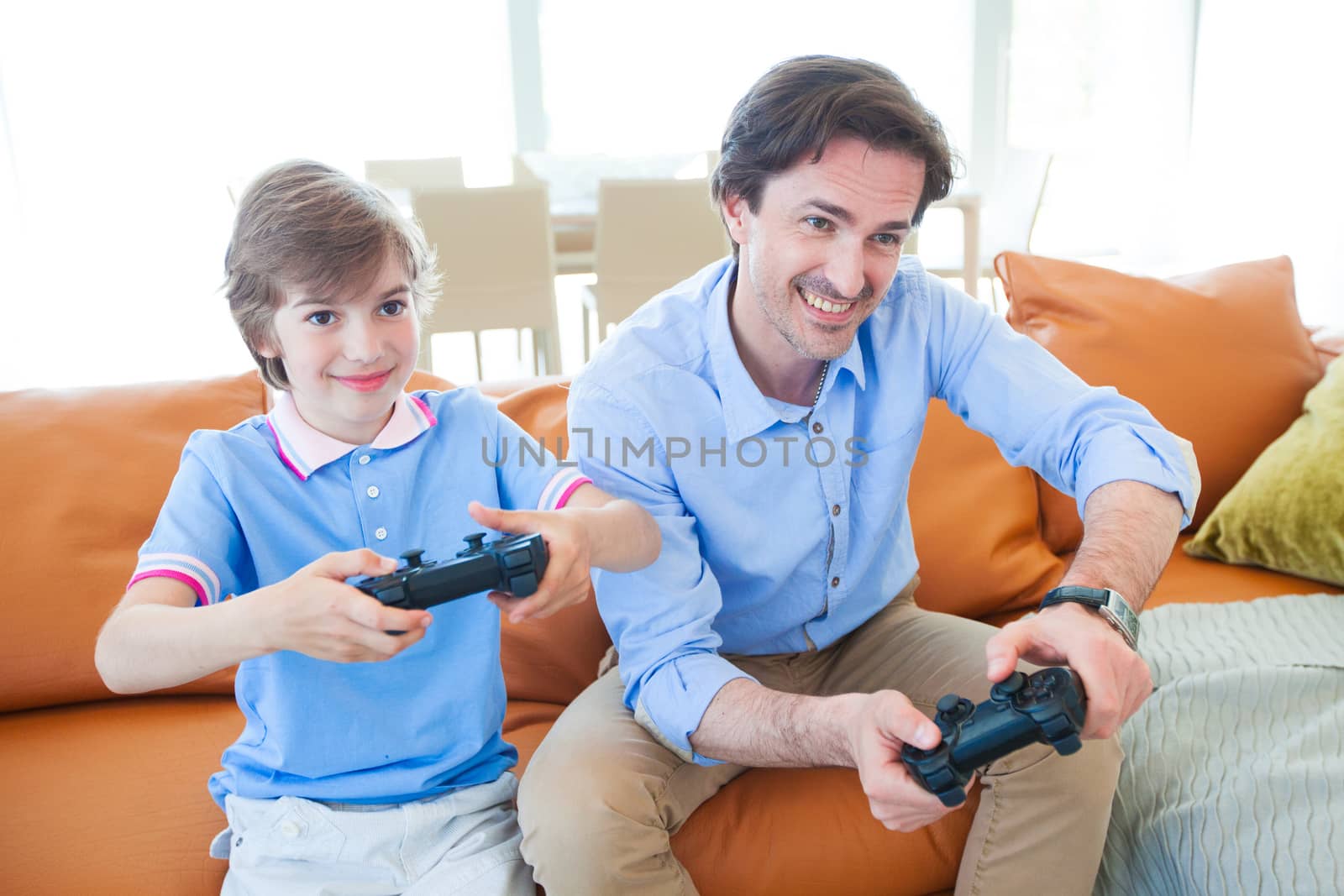 Father and son sitting on sofa in lounge playing video game