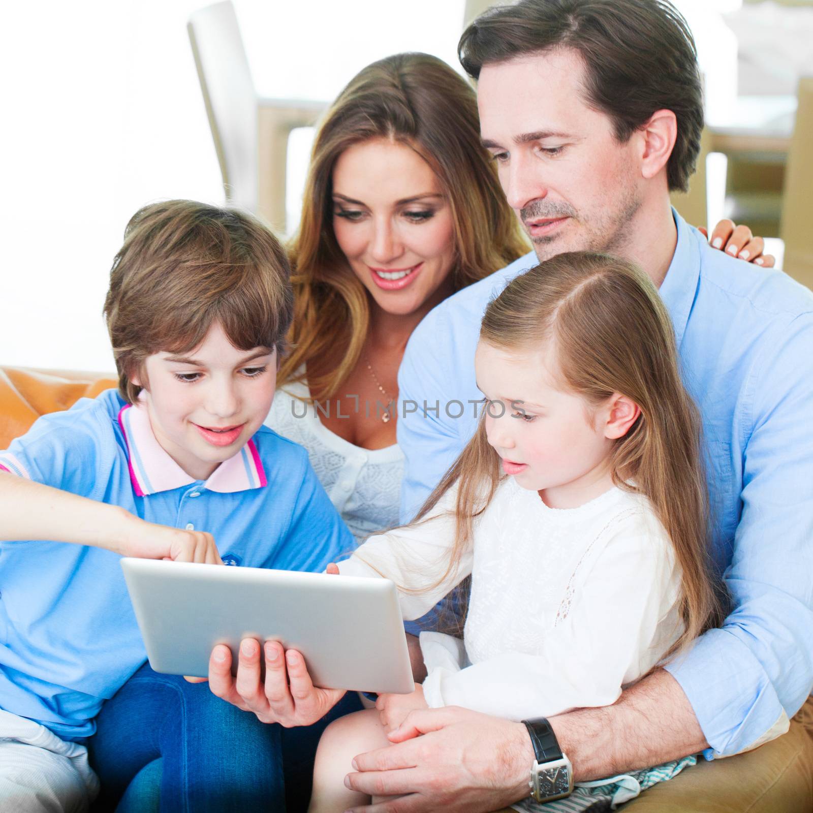 Portrait of happy family with two children sitting on sofa and using digital tablet pc