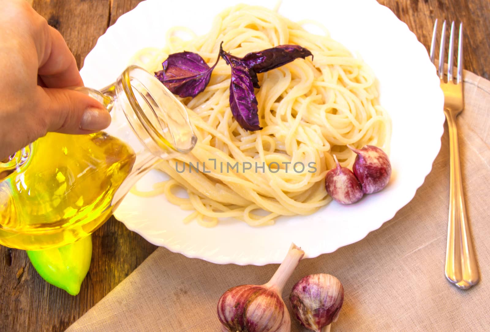 Italian cuisine, spaghetti with Basil and garlic, a woman's hand holding a glass jug of olive oil.