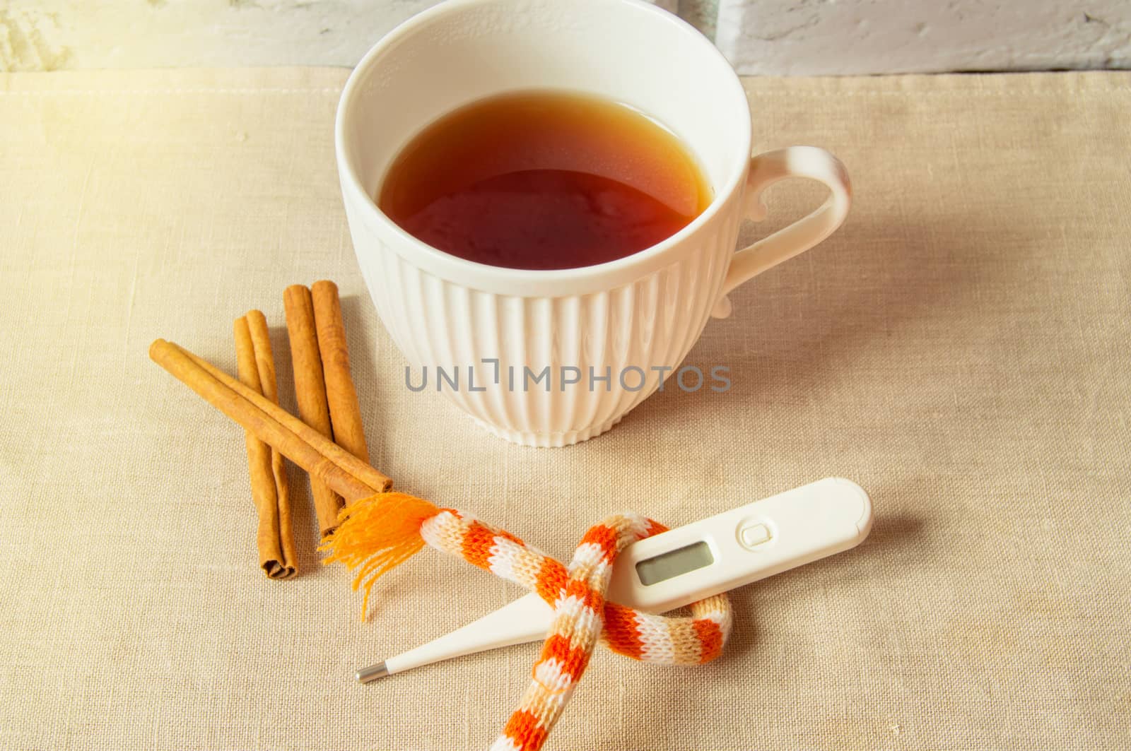 Concept of treating colds - hot tea with cinnamon, thermometer and scarf.