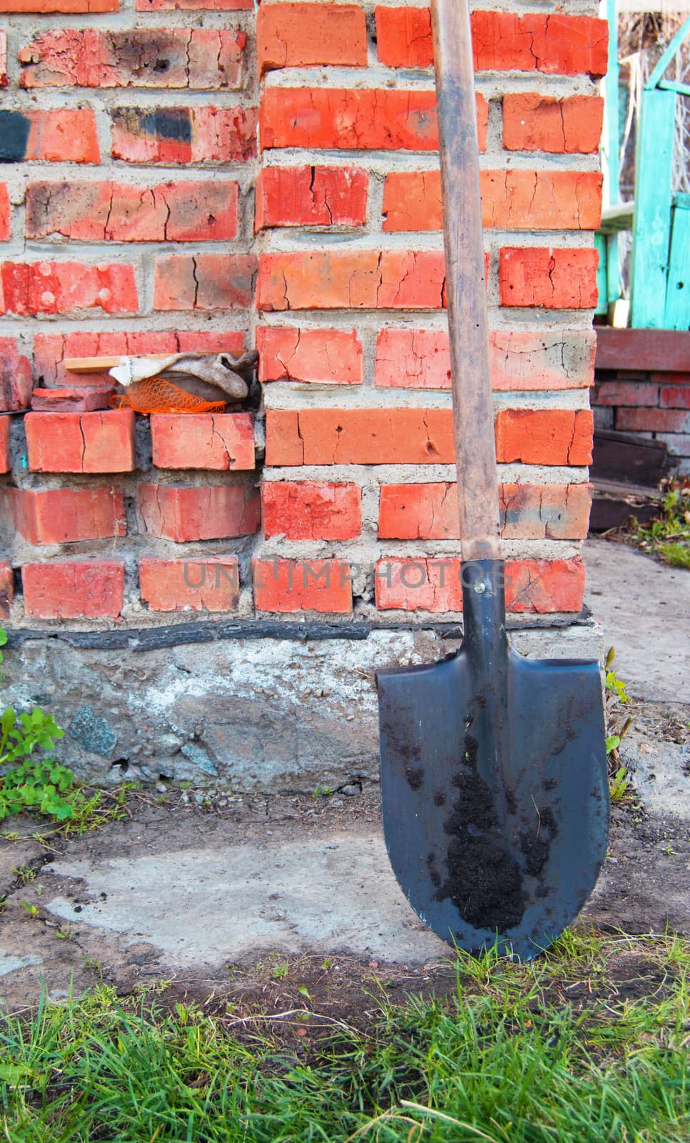 Metal shovel with wooden handle is a brick wall of the rural house.