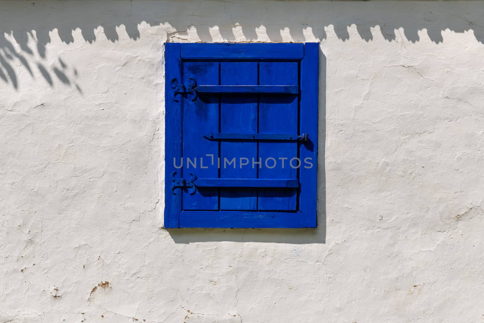 Detail of a traditional village window in Romania painted in strident blue on a white mud wall background.