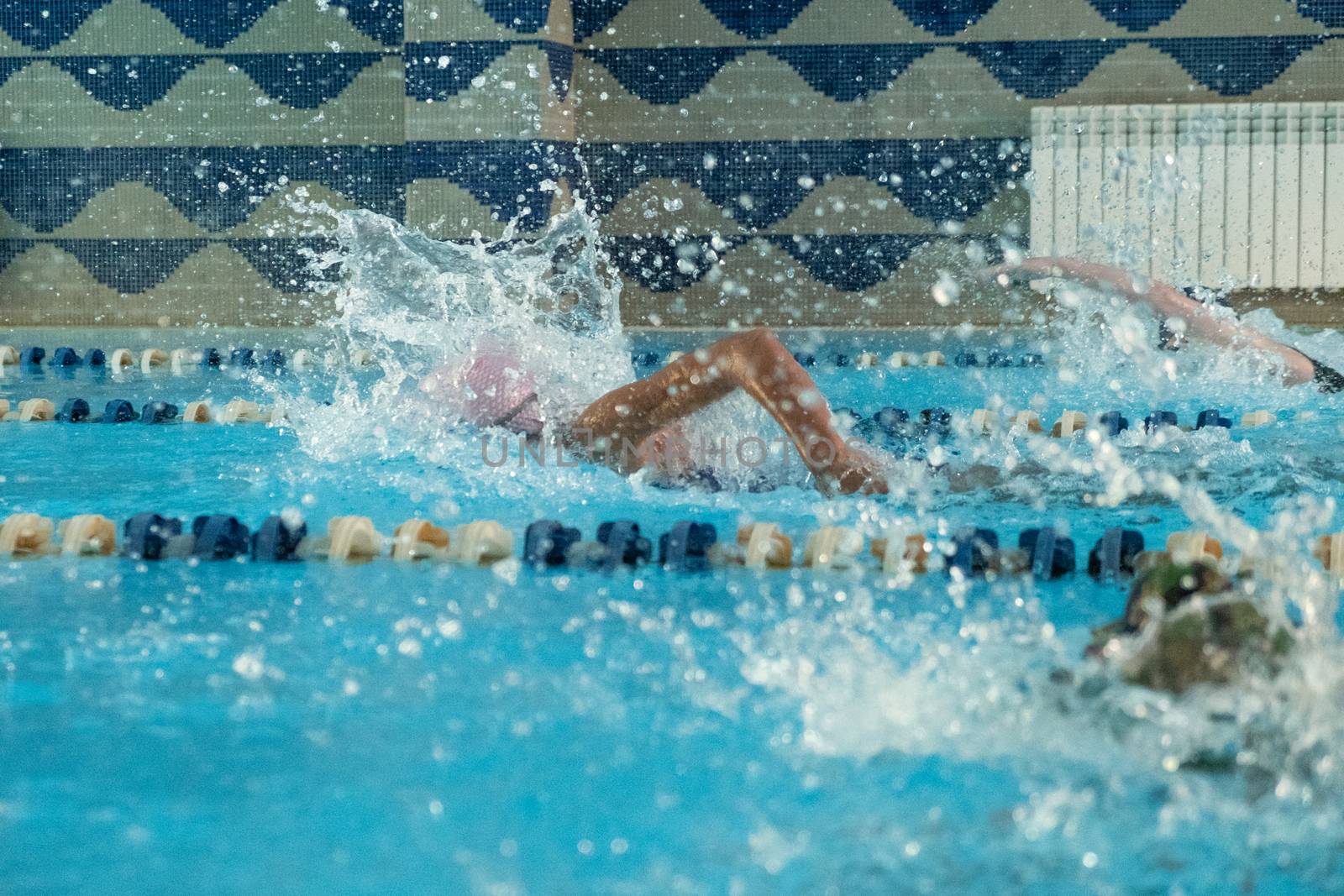 Children swimming freestyle. Indoor swimming pool with clear blue water.