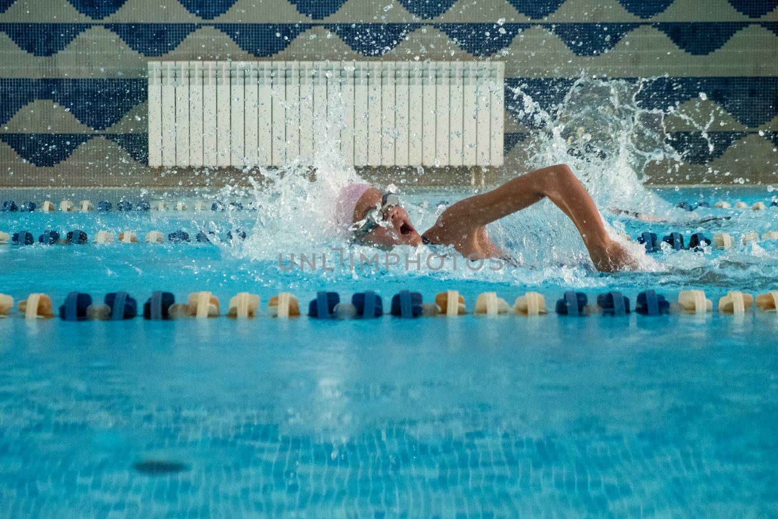 Children swimming freestyle. Indoor swimming pool with clear blue water.