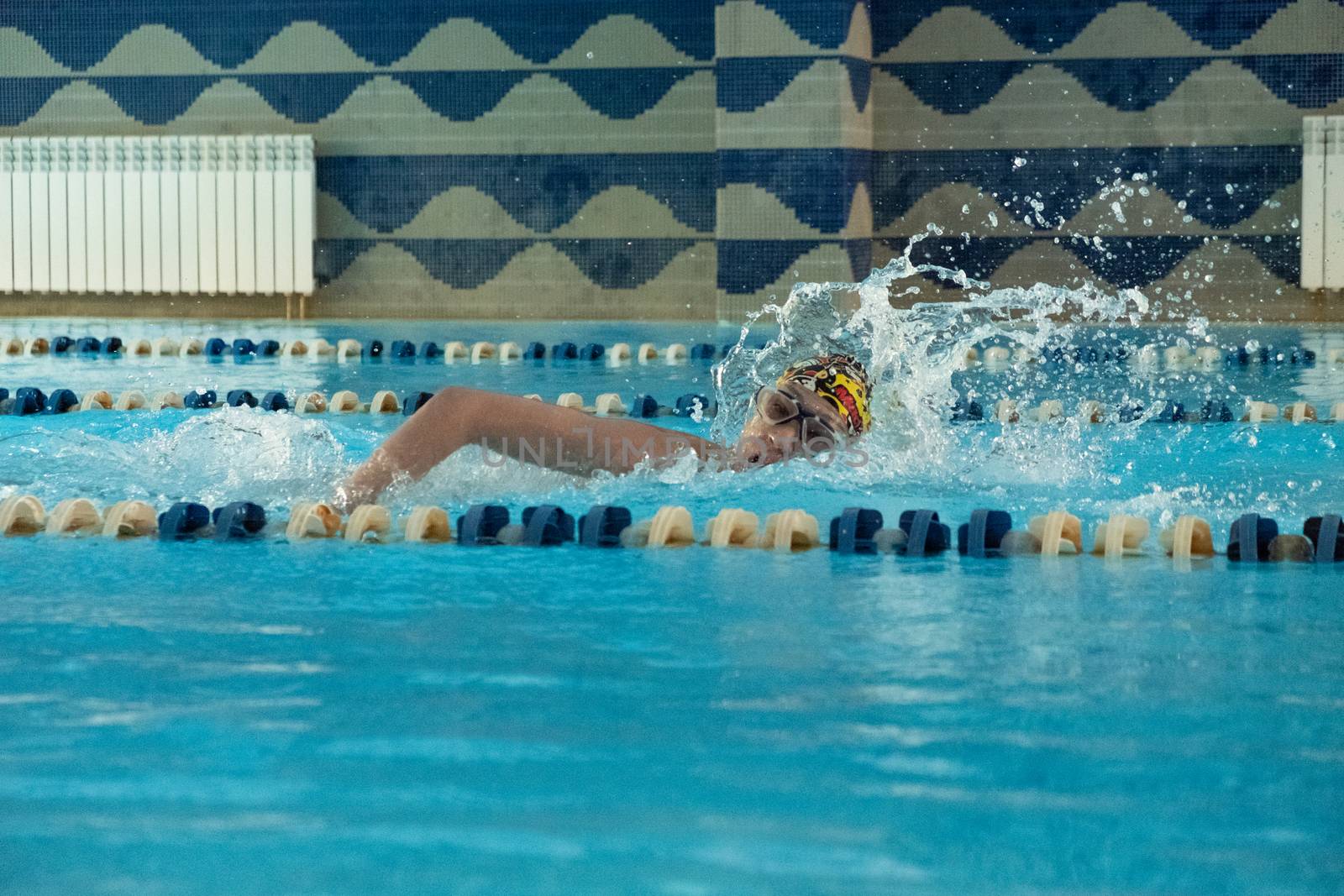 Children swimming freestyle. Indoor swimming pool with clear blue water.