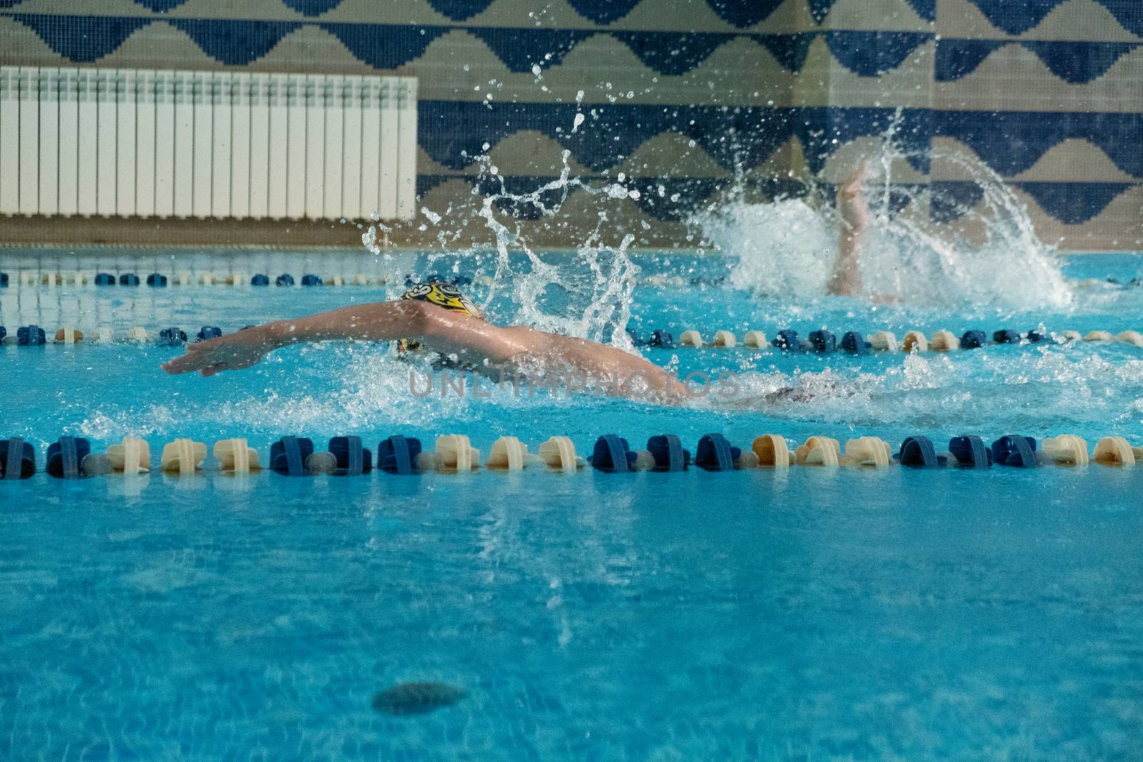 Children swimming freestyle. Indoor swimming pool with clear blue water.