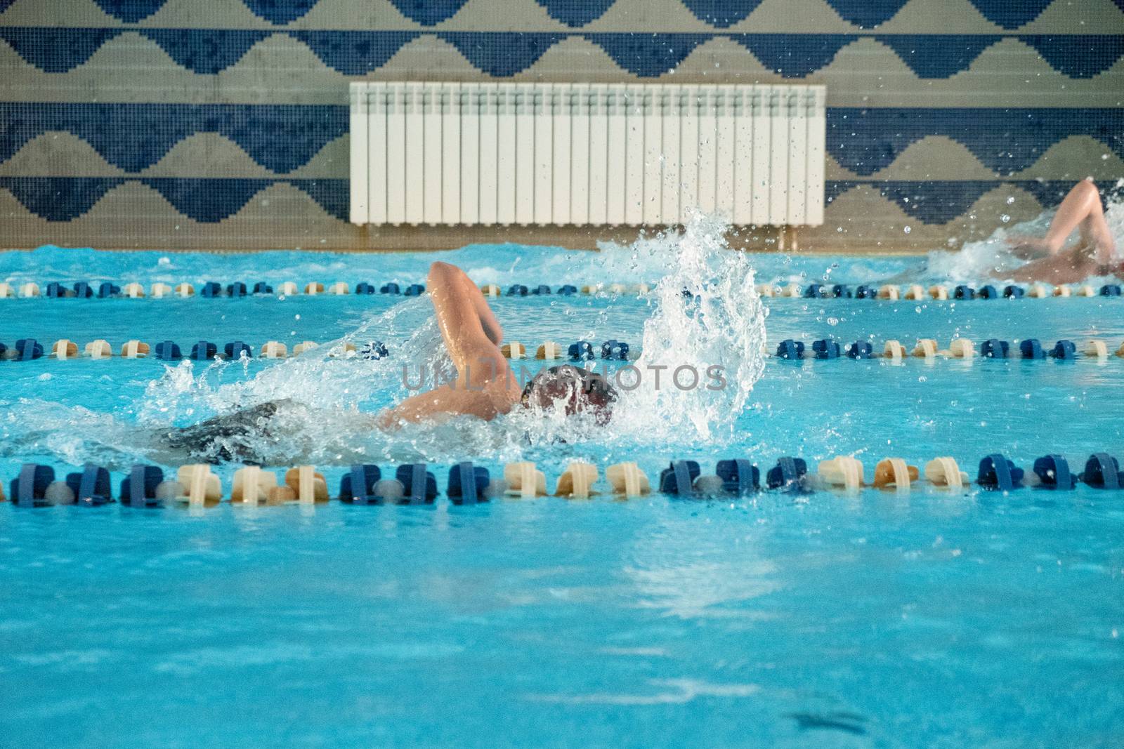 Children swimming freestyle. Indoor swimming pool with clear blue water.