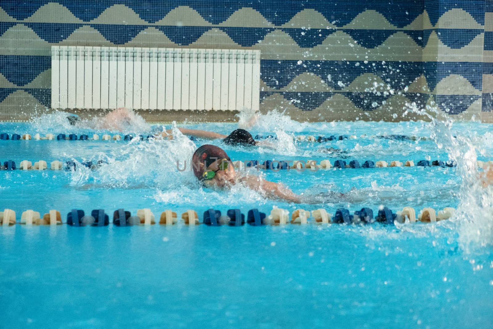 Children swimming freestyle. Indoor swimming pool with clear blue water.