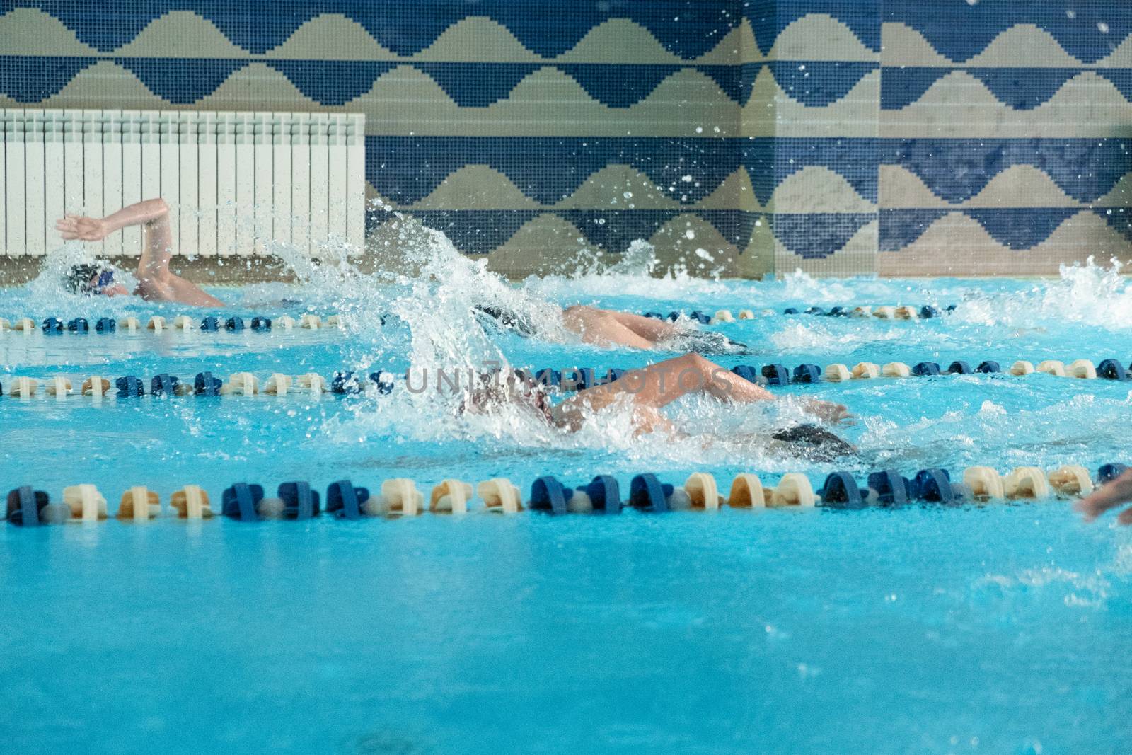 Children swimming freestyle. Indoor swimming pool with clear blue water.