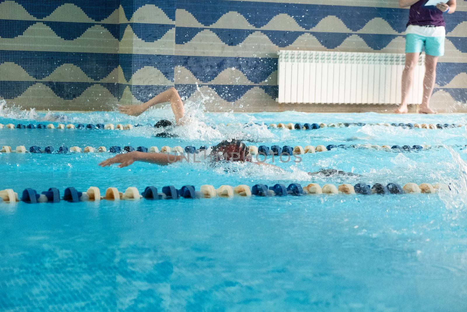 Children swimming freestyle. Indoor swimming pool with clear blue water.