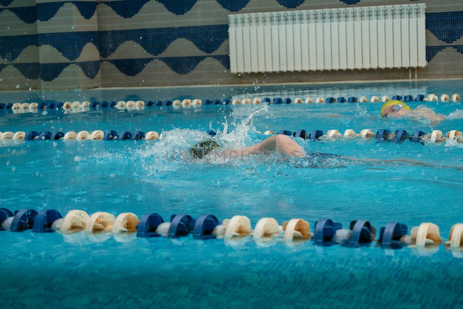 Children swimming freestyle. Indoor swimming pool with clear blue water.