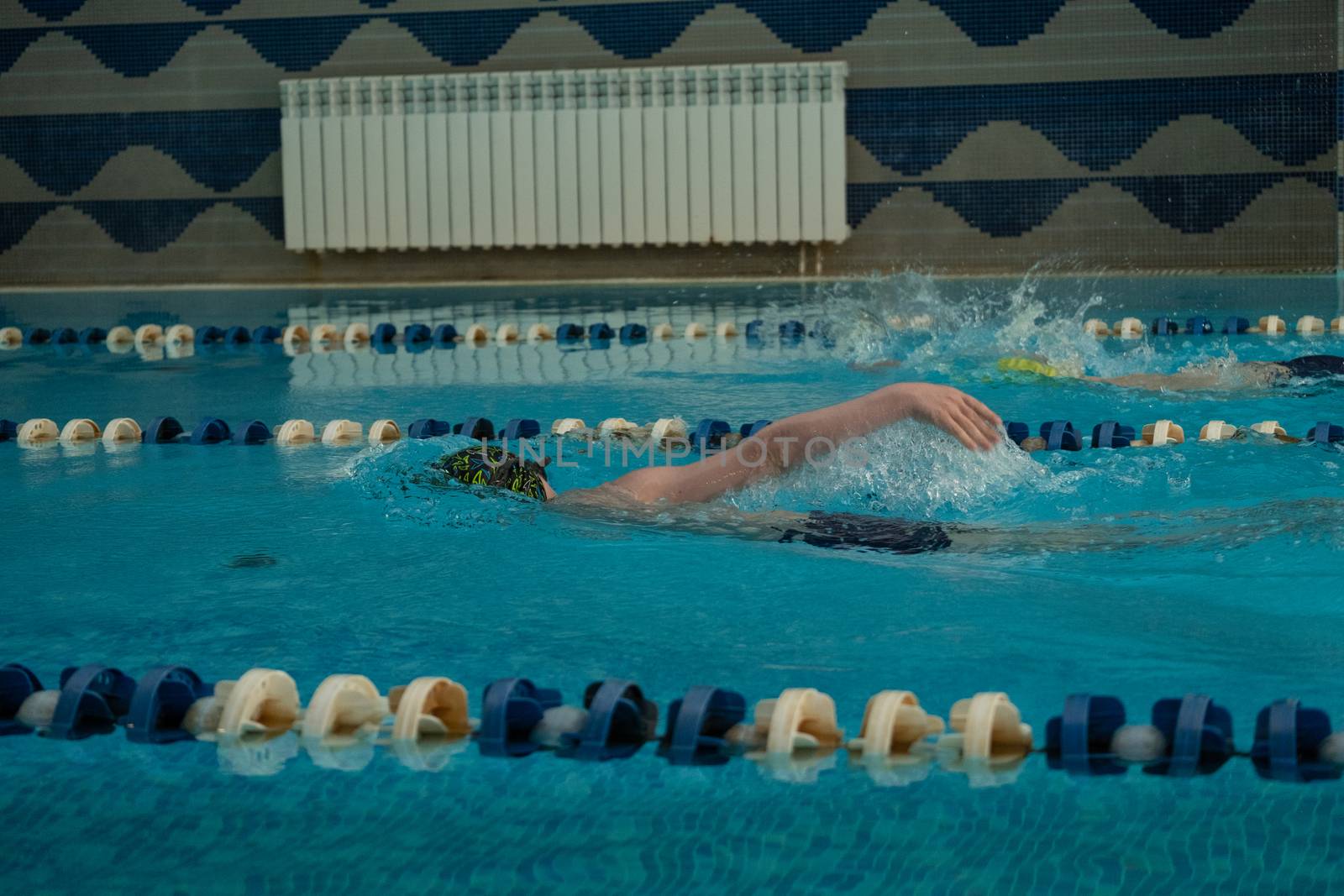 Children swimming freestyle. Indoor swimming pool with clear blue water.