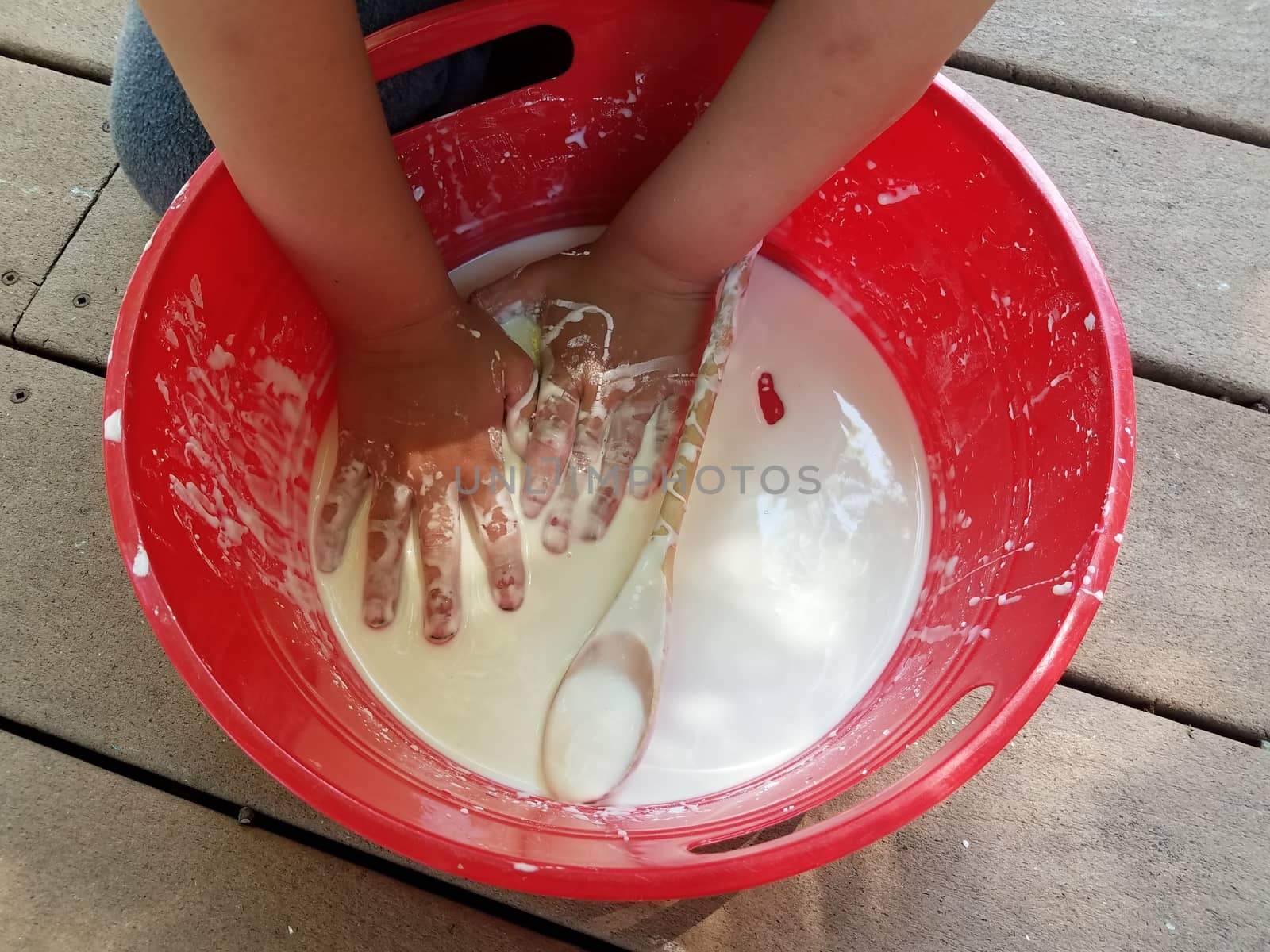 kid with hands playing in red bucket with white slime and wooden spoon on deck