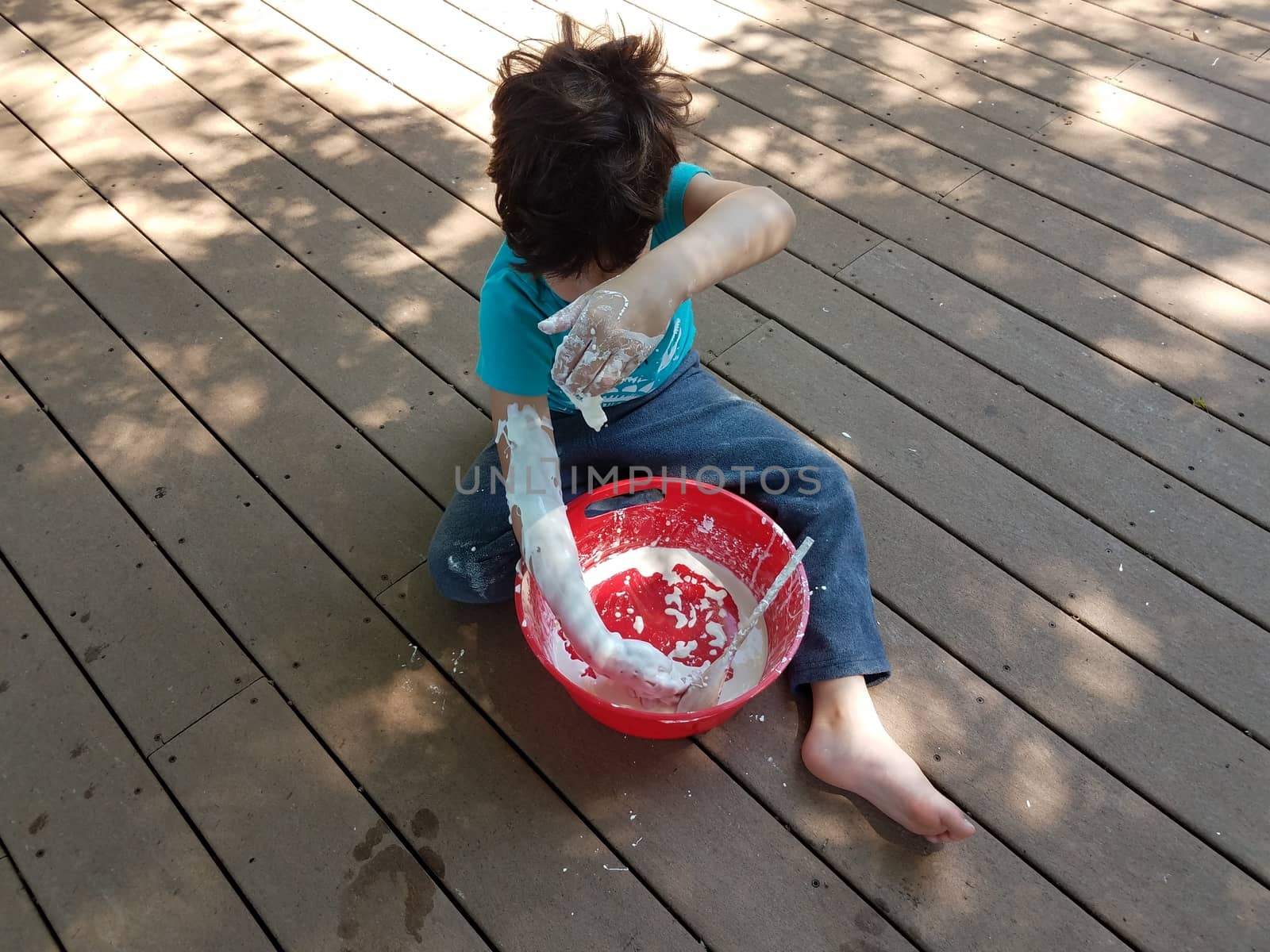 boy playing in red bucket with white slime and wooden spoon on deck