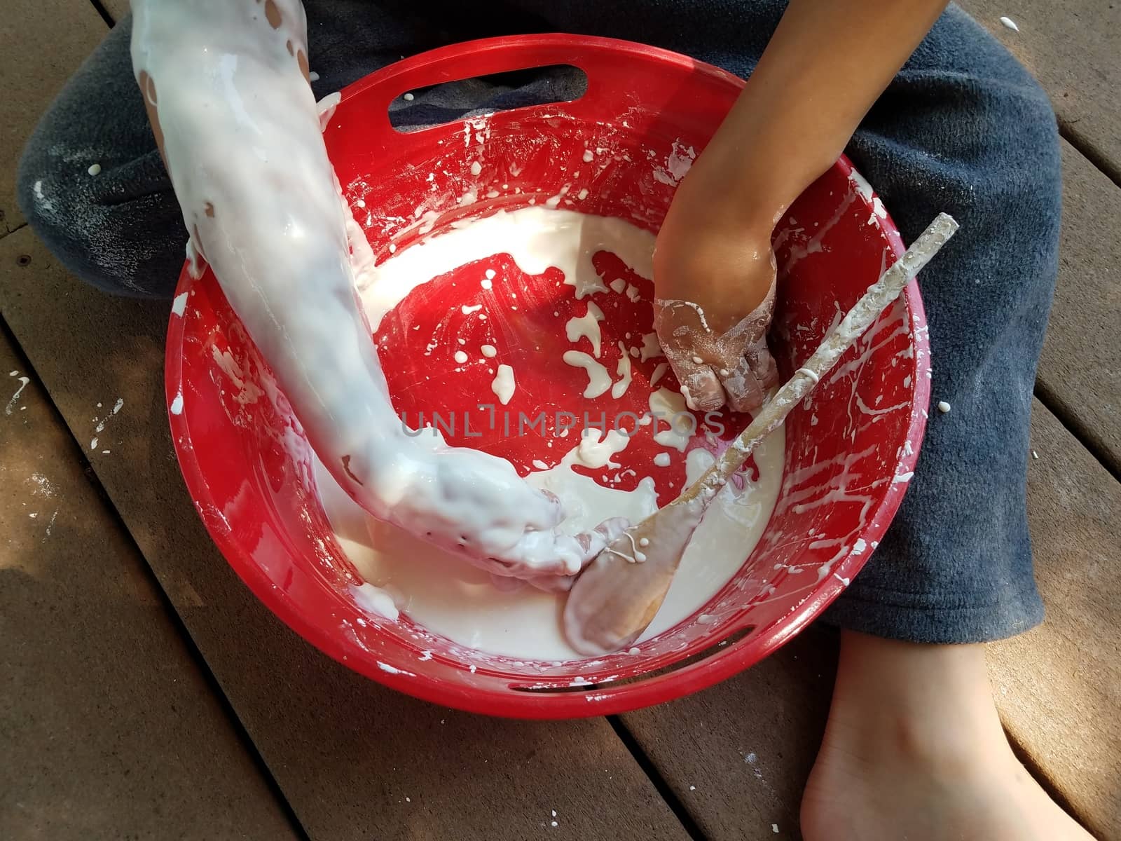 kid with hands playing in red bucket with white slime on deck by stockphotofan1