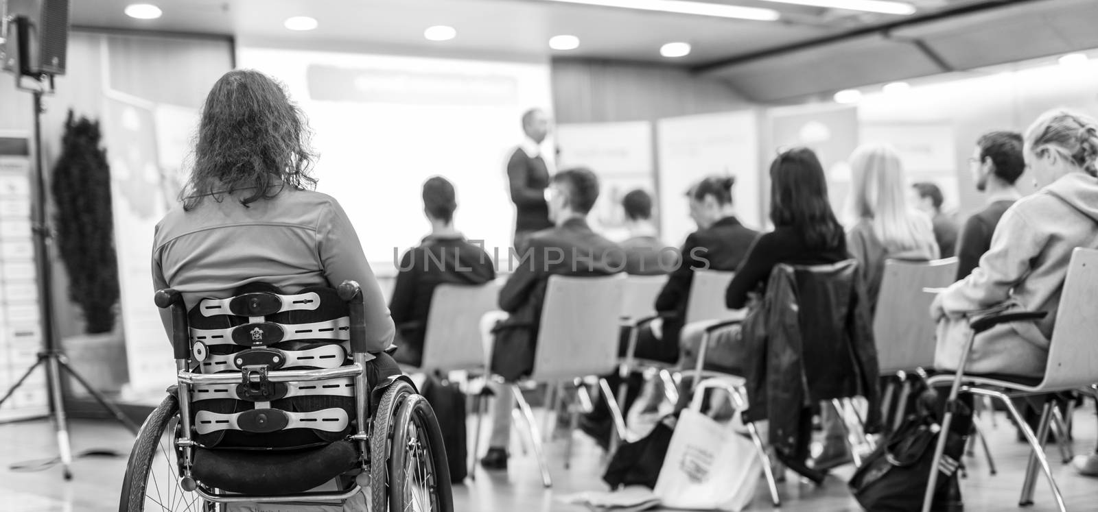 Rear view of unrecognizable woman on wheelchair participating in business conference talk. Business and entrepreneurship symposium. Black and white image.