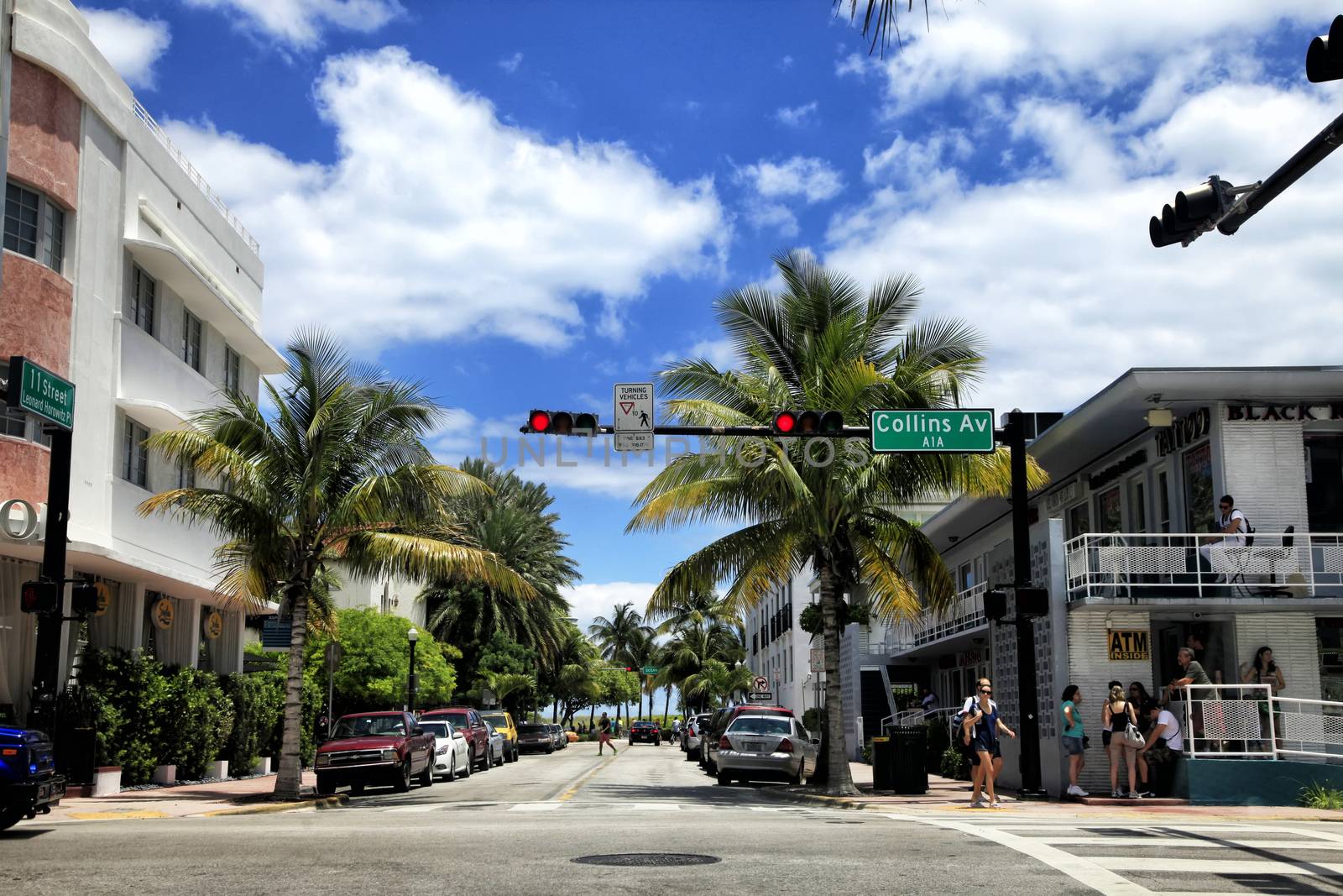 Miami Beach, Florida, USA - May 05, 2013: View along the famous vacation and tourist location on crossing Collins avenue and 11 street in district of South Beach, Miami on a sunny day with cars, palm trees and people visible.