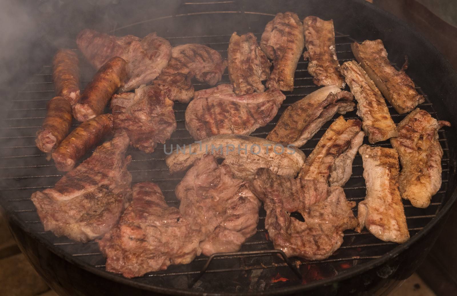 Grilling meats outdoors in a rustic old iron grill an hot coals for family gathering.