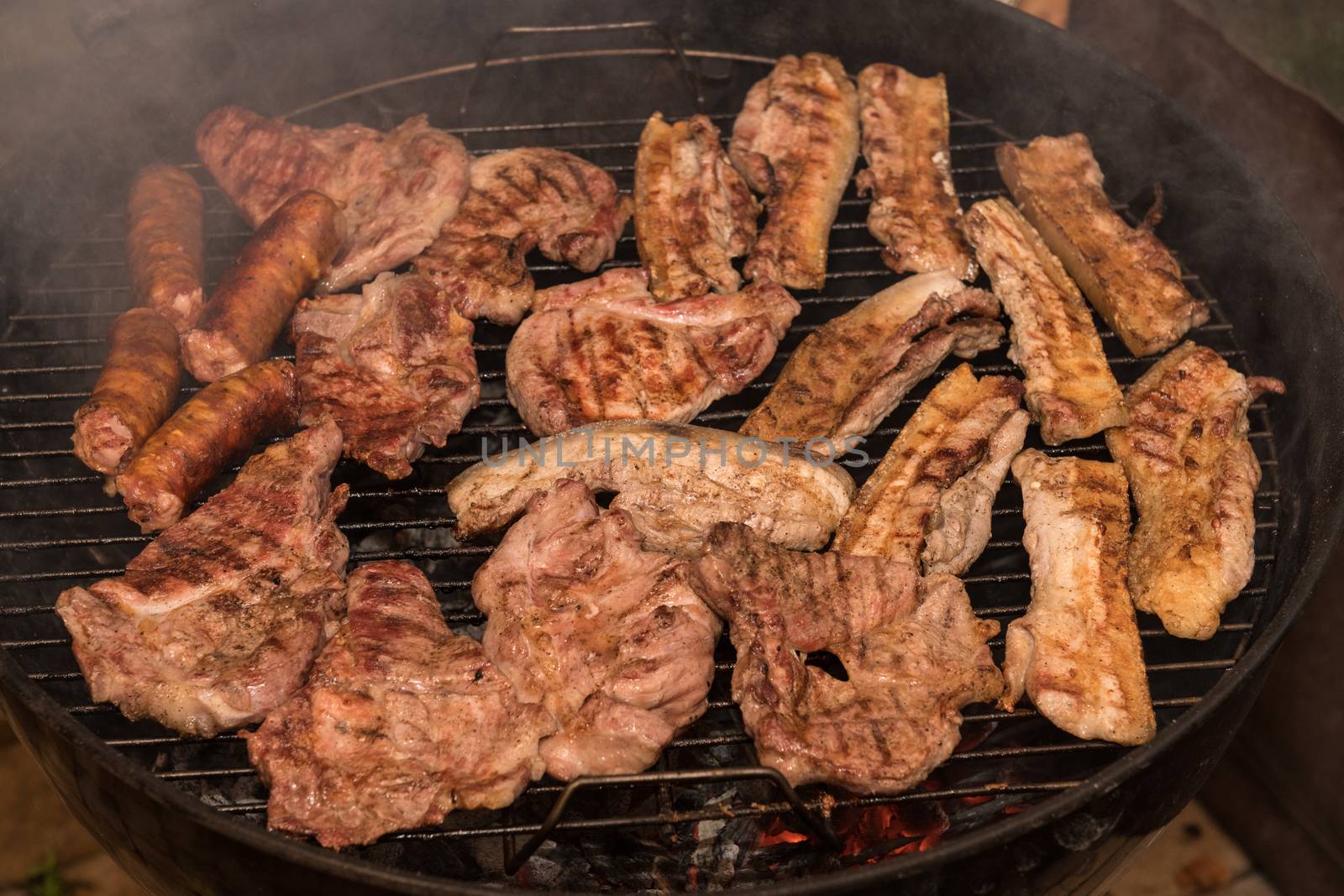 Grilling meats outdoors in a rustic old iron grill an hot coals for family gathering.