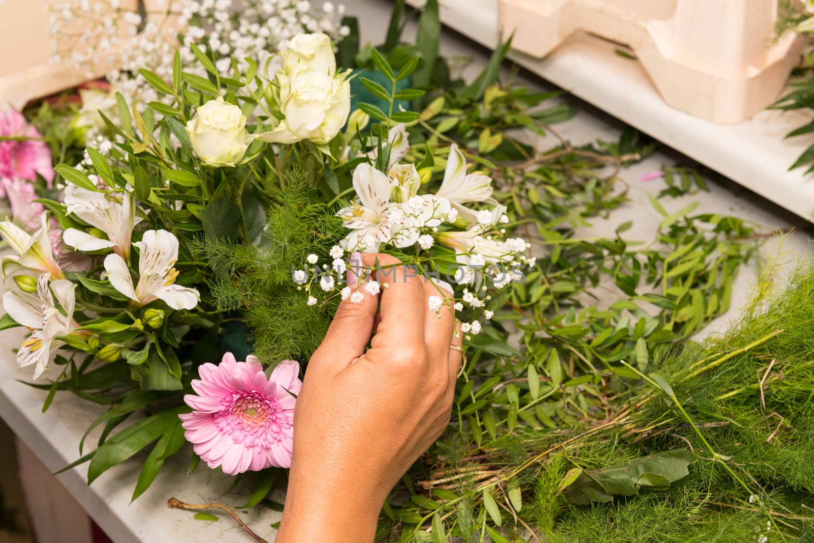 Florist female making a bouquet of different flowers at working table.