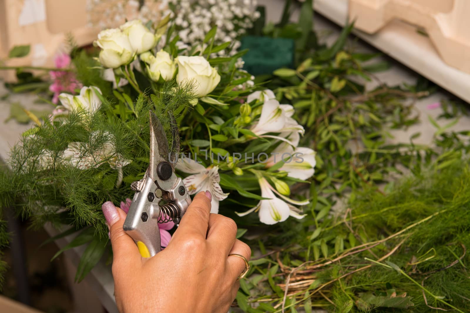 Florist female making a bouquet of different flowers at working table.