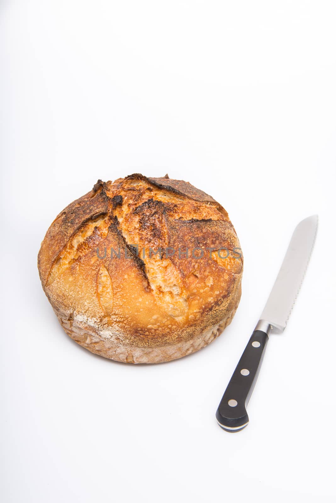 A fresh loaf of round artisan sourdough bread with a breaqd knife.