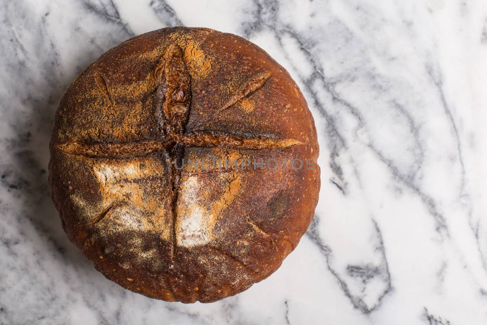 Homemade sourdough bread made in traditional style during Easter or other Christian Holidays with a simple cross signifying that bread is the body of Christ with copy space.